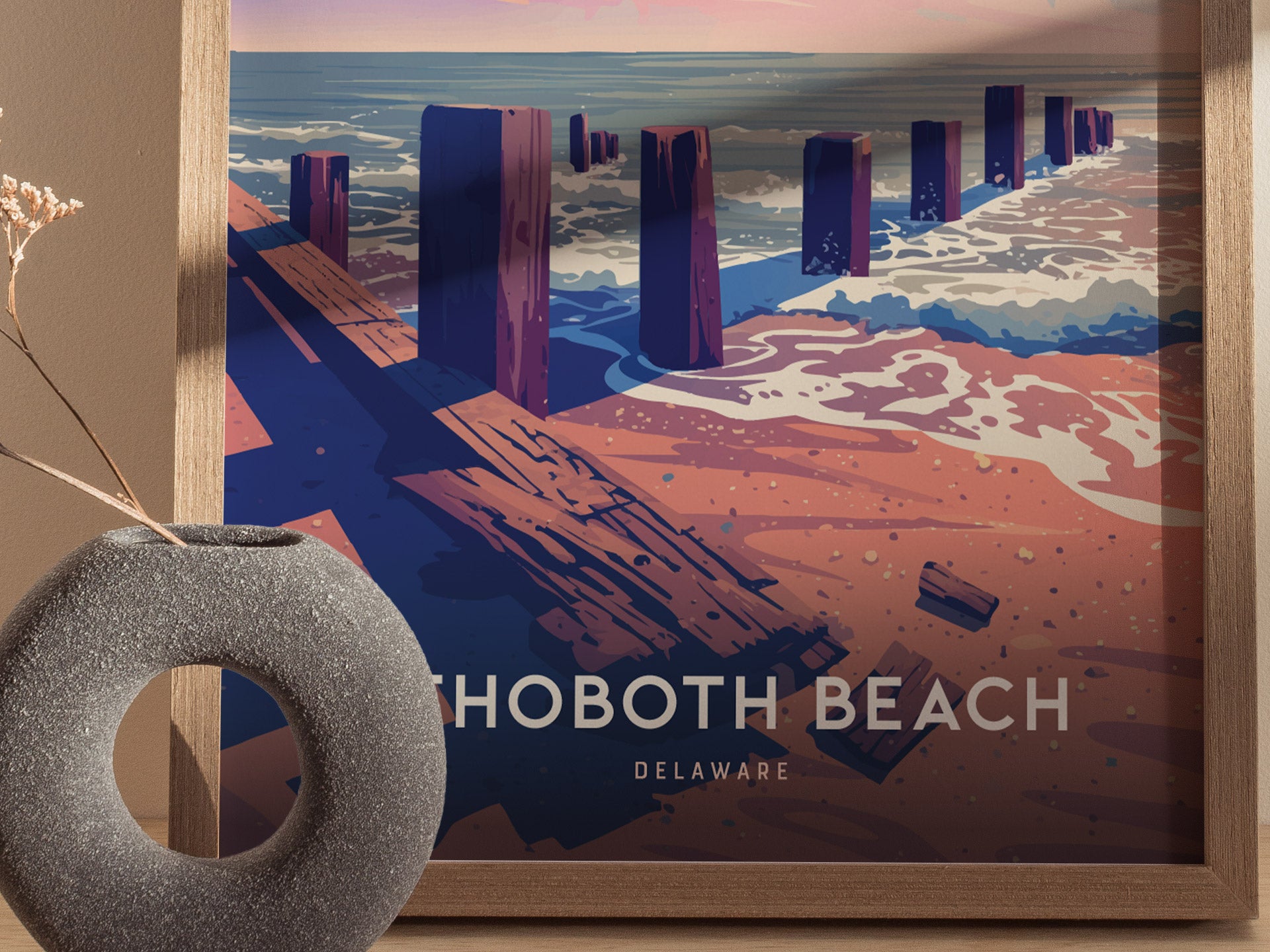 A framed poster of Rehoboth Beach, Delaware, features stylized wooden posts along a sandy shore with ocean waves. A textured gray vase sits nearby, adding a decorative touch.