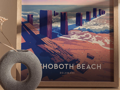 A framed poster of Rehoboth Beach, Delaware, features stylized wooden posts along a sandy shore with ocean waves. A textured gray vase sits nearby, adding a decorative touch.