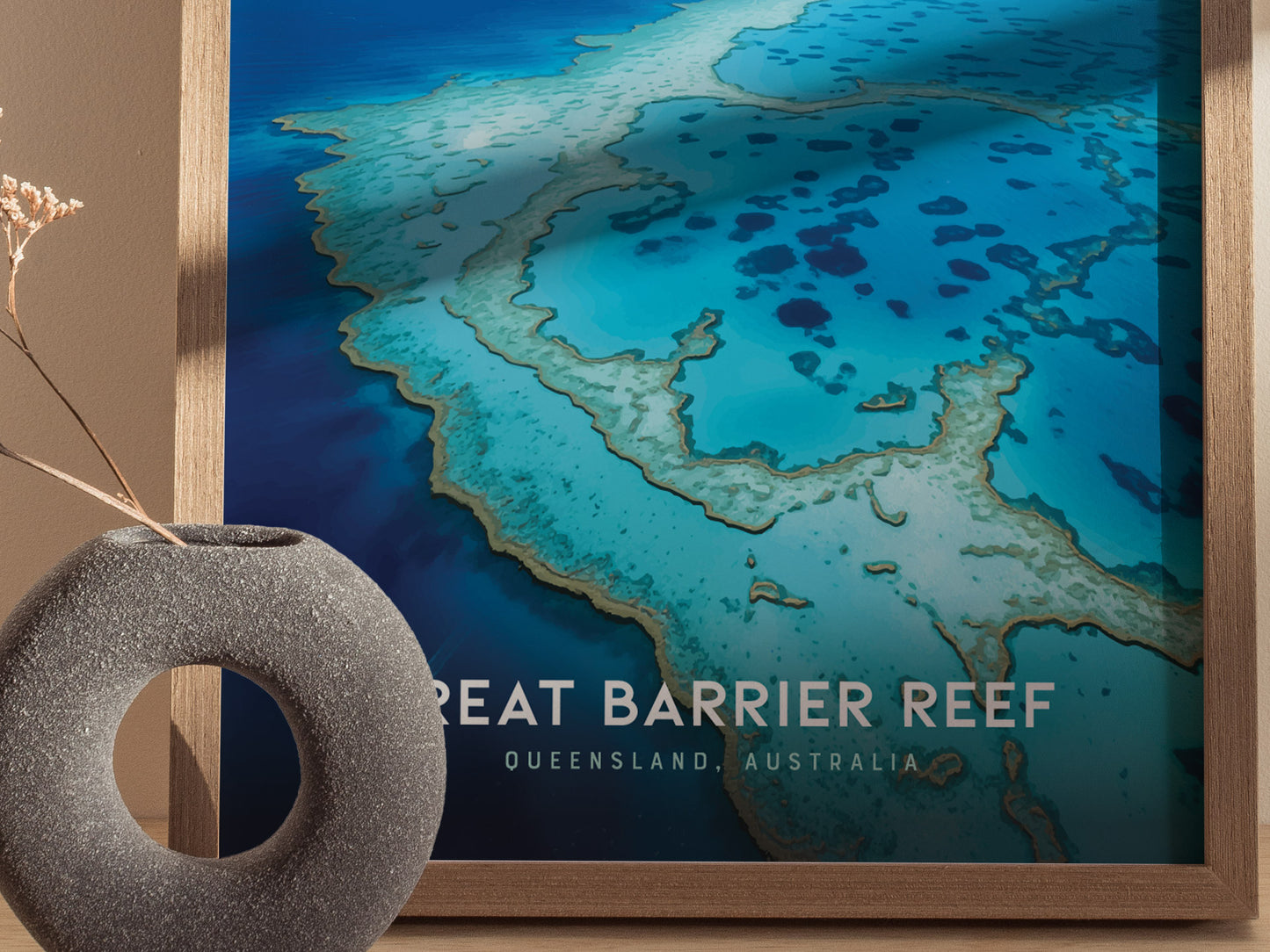 A framed poster of the Great Barrier Reef with vibrant blue and turquoise waters is displayed next to a gray, circular vase on a wooden surface.