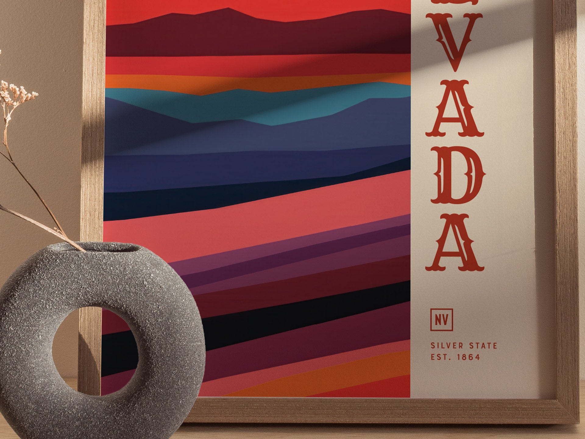 A minimalist Nevada poster features colorful abstract desert landscapes with bold NEVADA text on the side, framed in wood. A textured round vase with dried flowers is nearby.
