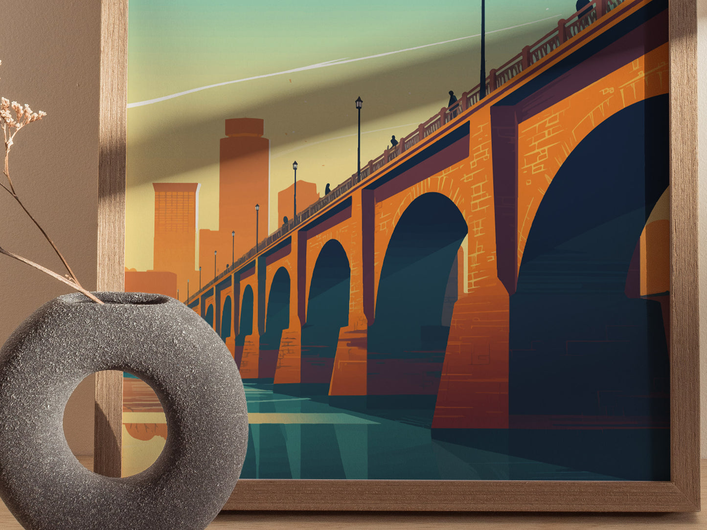 A framed poster depicts the Stone Arch Bridge over the Mississippi River with a stylized Minneapolis skyline in the background. A round stone vase is visible in the foreground.