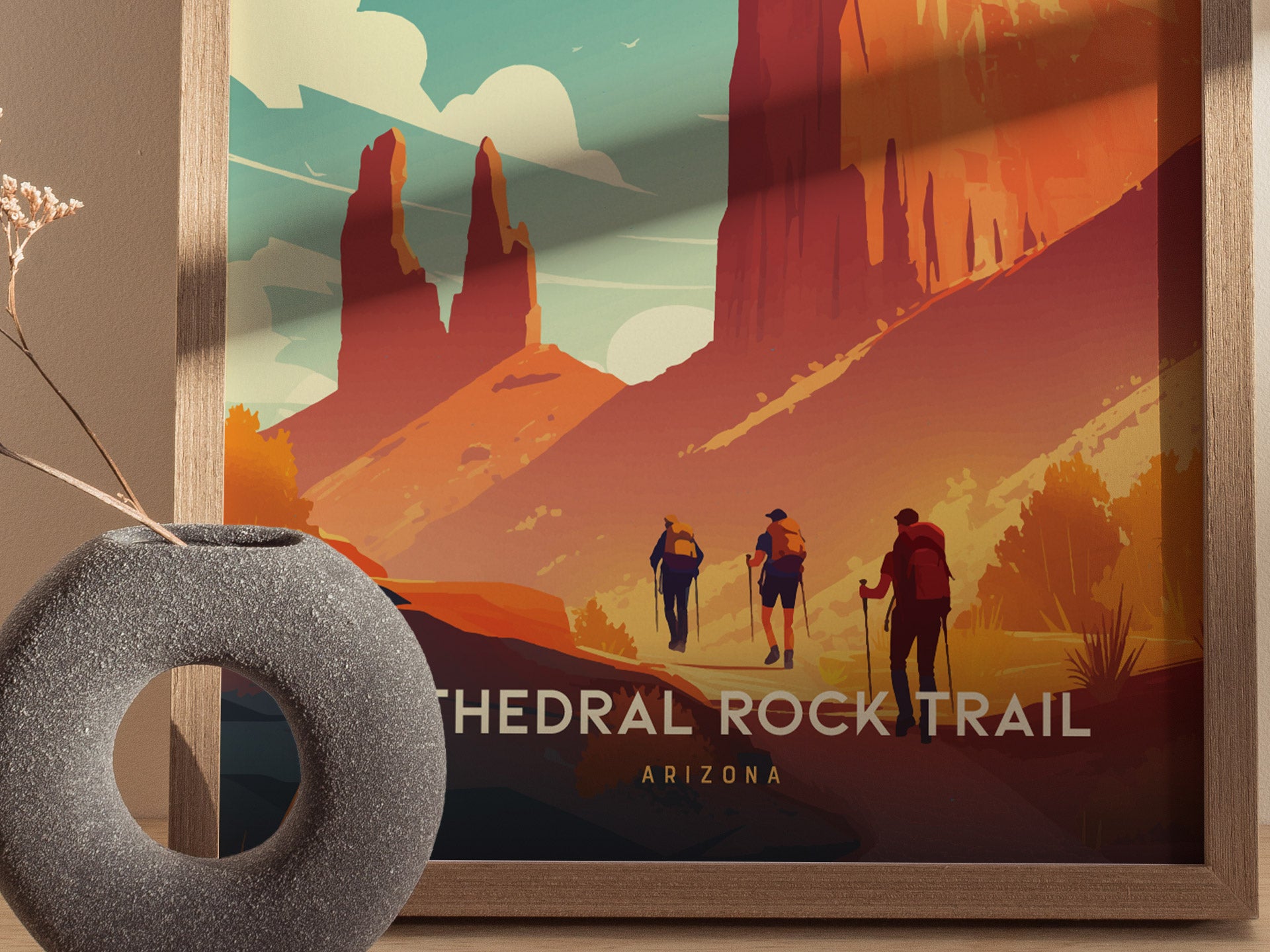 A framed poster of Cathedral Rock Trail in Sedona, Arizona, features vibrant red cliffs and hikers against a colorful sky. A gray vase with dried flowers is in the foreground.