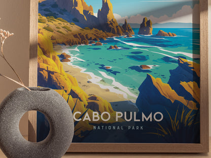 A framed poster of Cabo Pulmo National Park features vibrant coastal cliffs and turquoise waters. A textured gray vase with dried flowers is placed in front of the artwork.