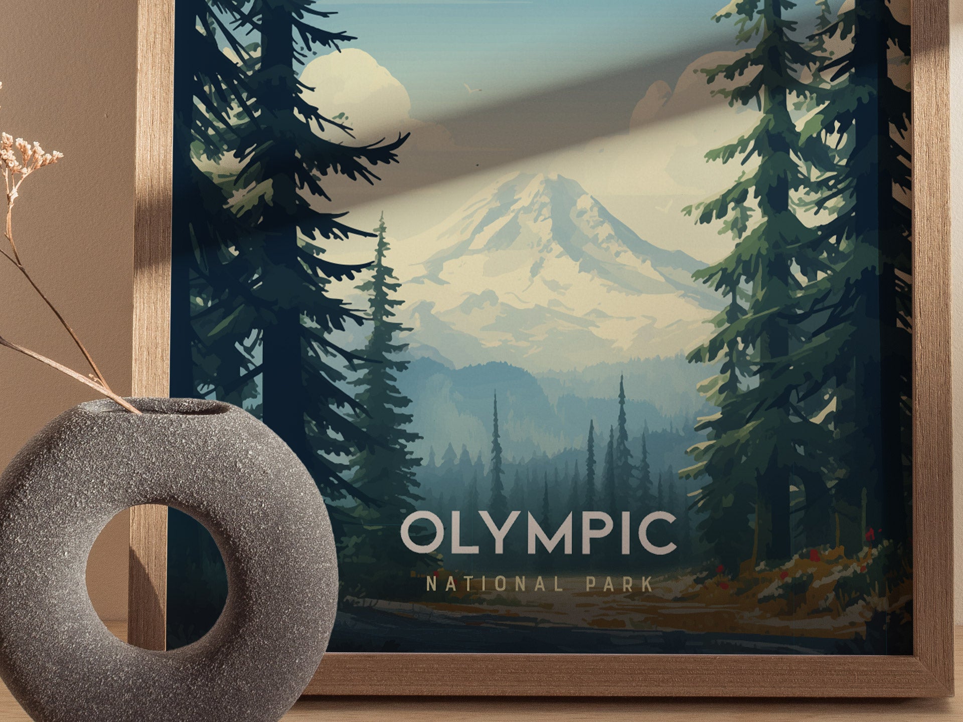 Framed poster of Olympic National Park featuring snow-capped mountains and dense evergreen trees, with soft lighting casting shadows. A textured vase with dried flowers sits nearby.