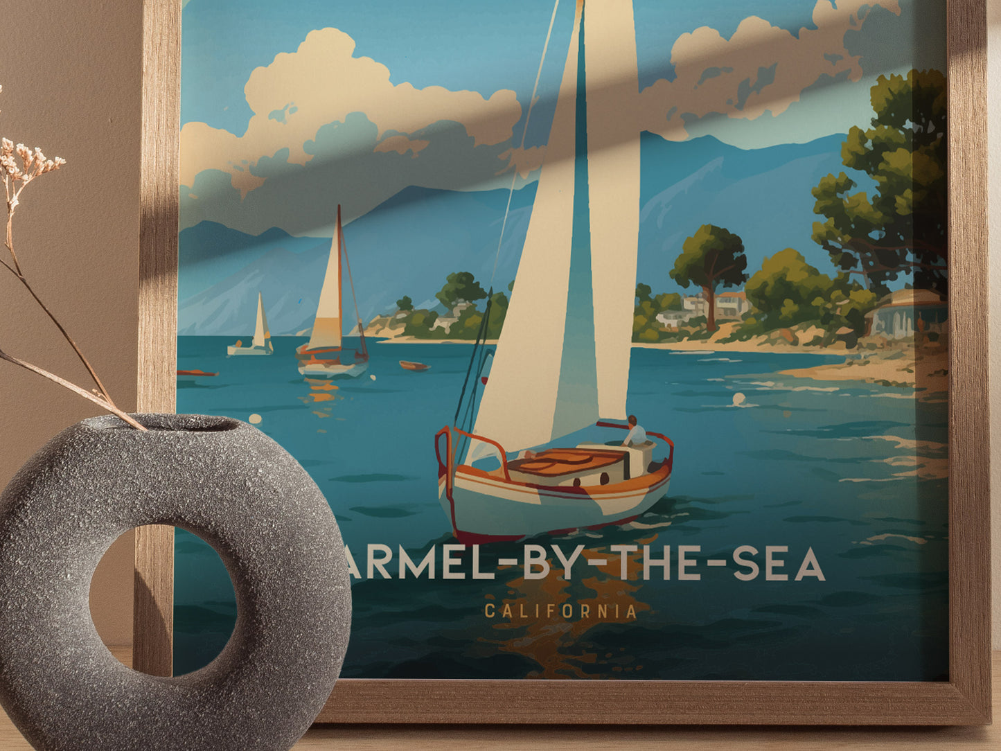 A framed poster depicts sailboats on a serene coastal scene in Carmel-by-the-Sea, California, with mountains and trees in the background. A decorative vase is placed nearby.