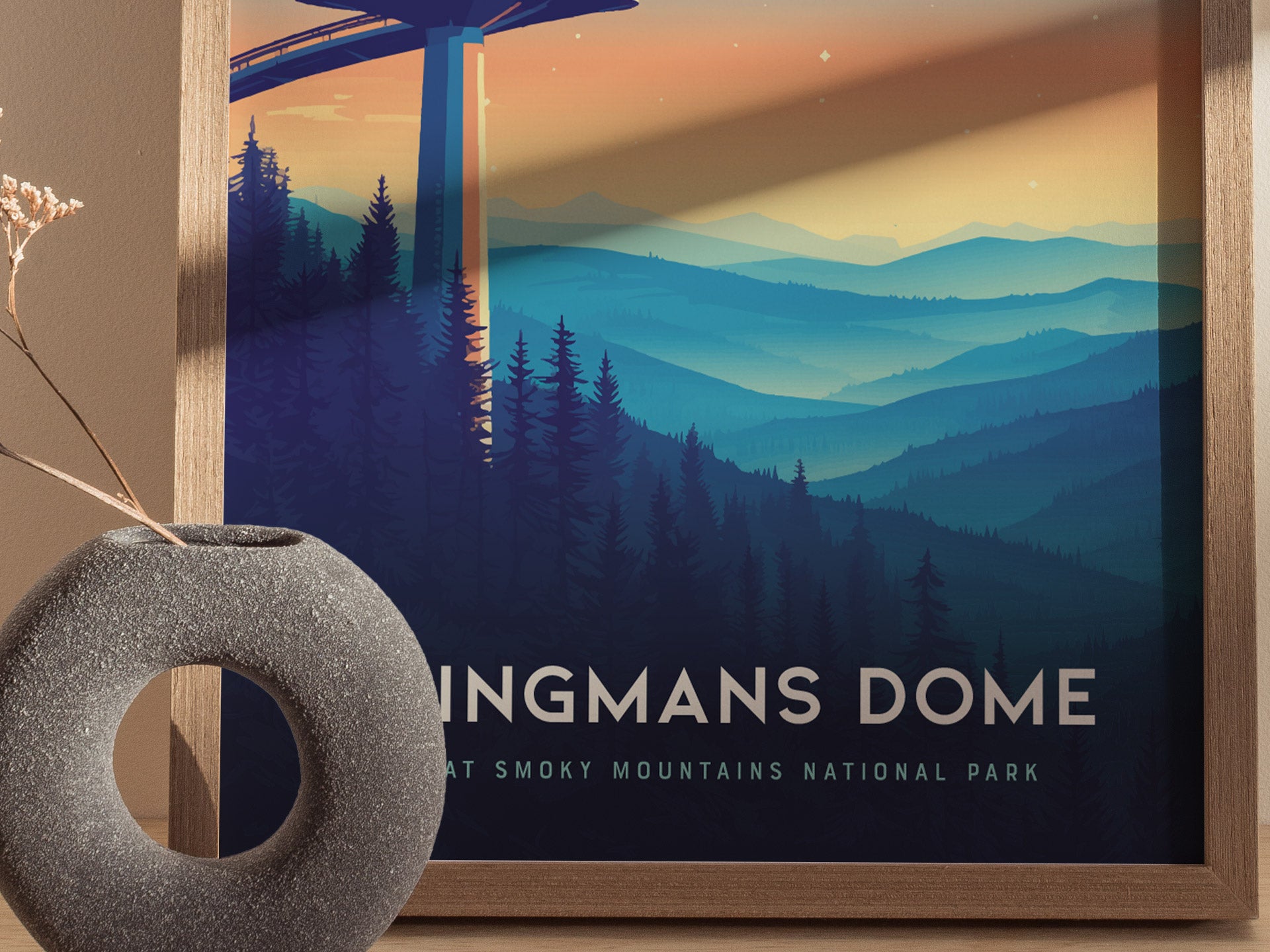A framed poster of Clingmans Dome showcases an illustration of the observation tower against a backdrop of layered blue mountain ridges under a gradient sky. A round stone vase with dried flowers is in the foreground.