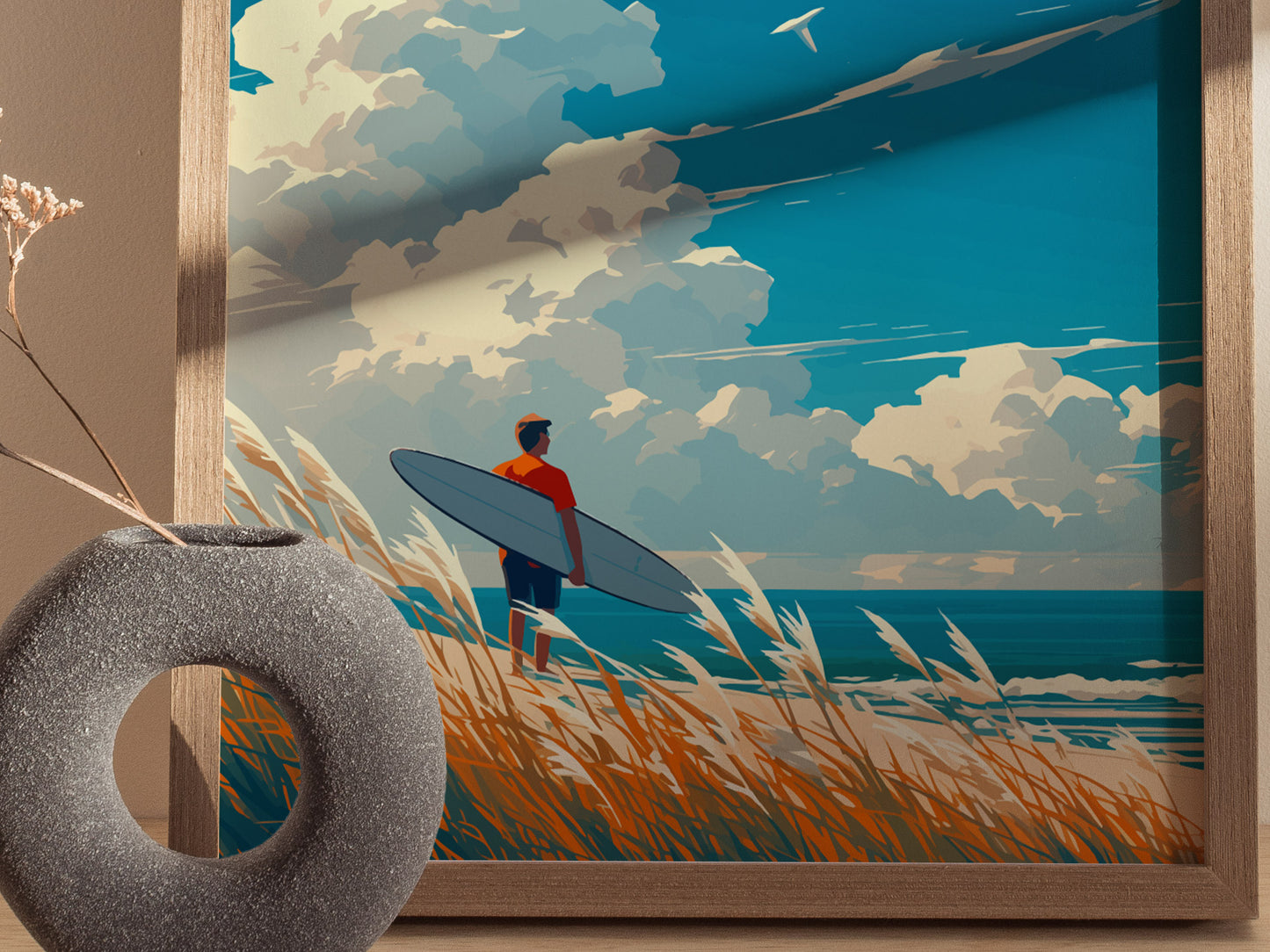 A framed artwork depicts a surfer with a board standing on a grassy dune, overlooking the ocean under a partly cloudy sky. A decorative vase is visible in the foreground.