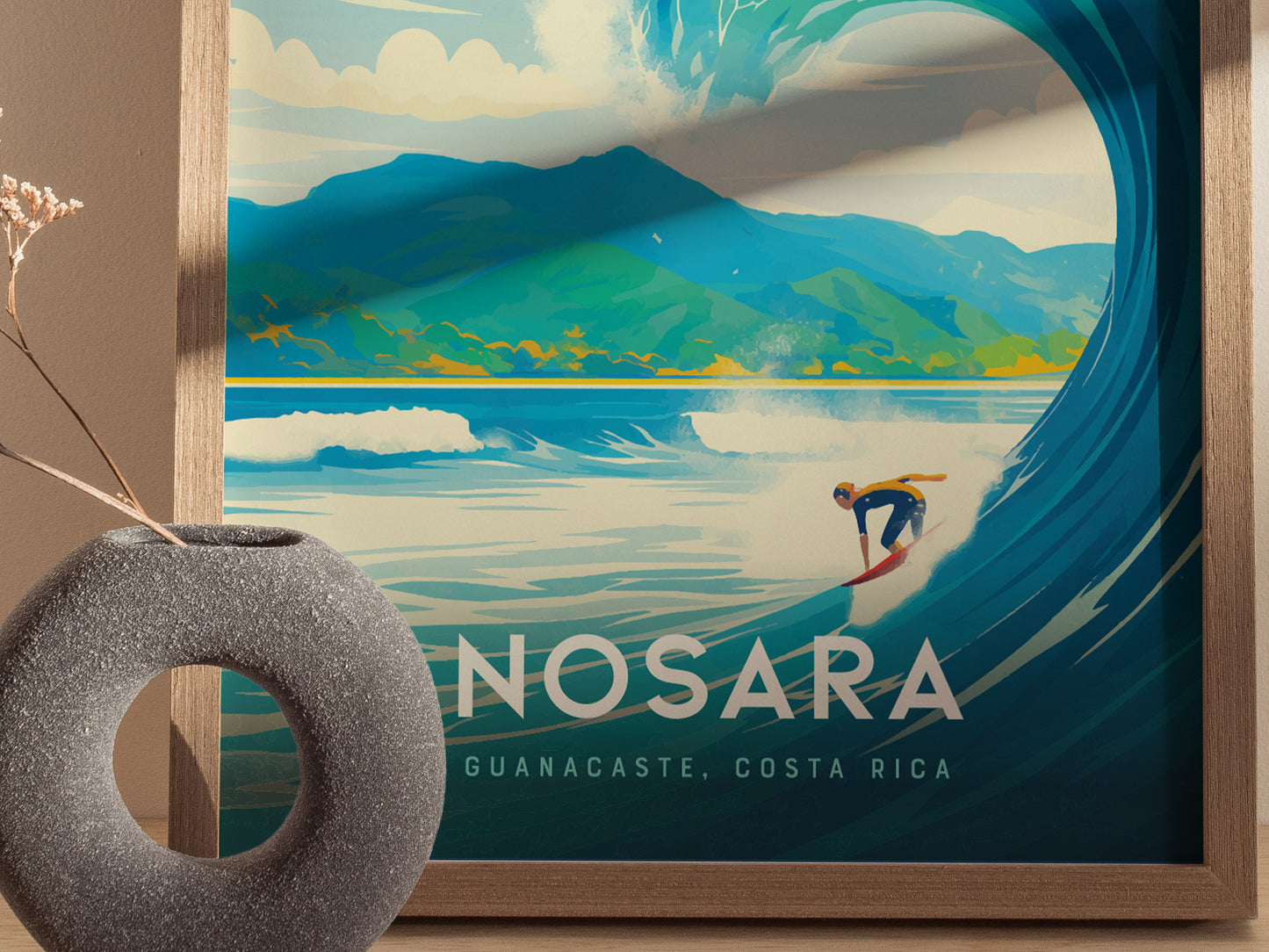 A framed poster of Nosara, Costa Rica features a surfer riding a large wave with lush green mountains in the background. A textured gray vase is placed nearby.