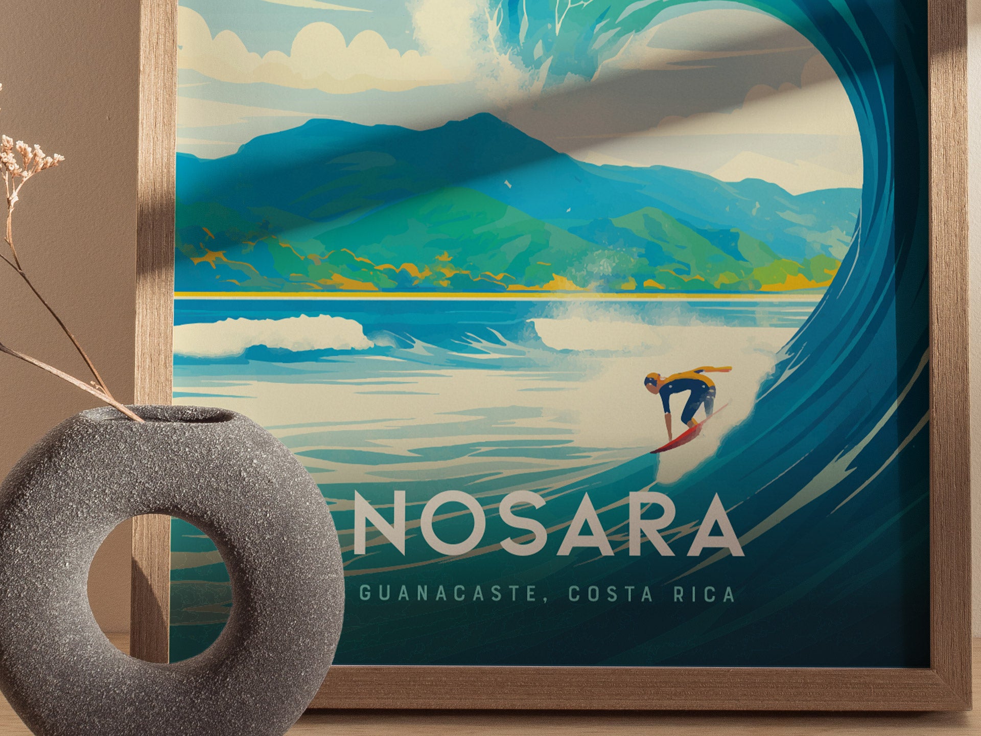 A framed poster of Nosara, Costa Rica features a surfer riding a large wave with lush green mountains in the background. A textured gray vase is placed nearby.