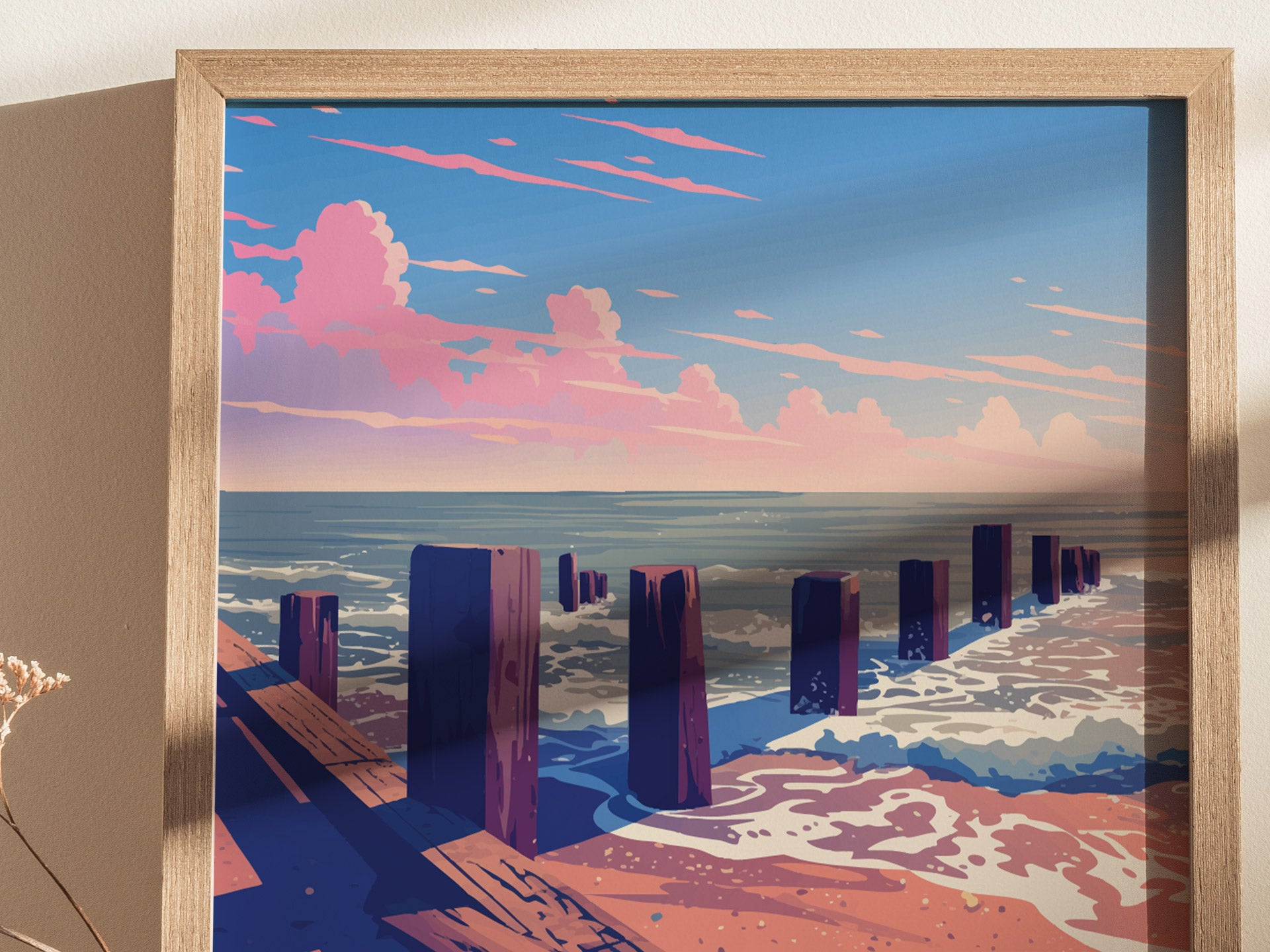 A framed artwork depicting a coastal scene with wooden posts in the sand, waves crashing, and a vibrant sunset sky with pink clouds over the ocean.