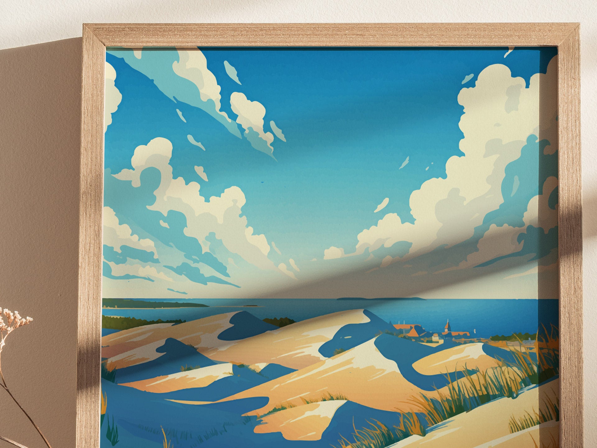 Framed artwork depicting a scenic view of sand dunes under a vibrant blue sky with fluffy clouds. In the distance, a small town and deep blue waters are visible.