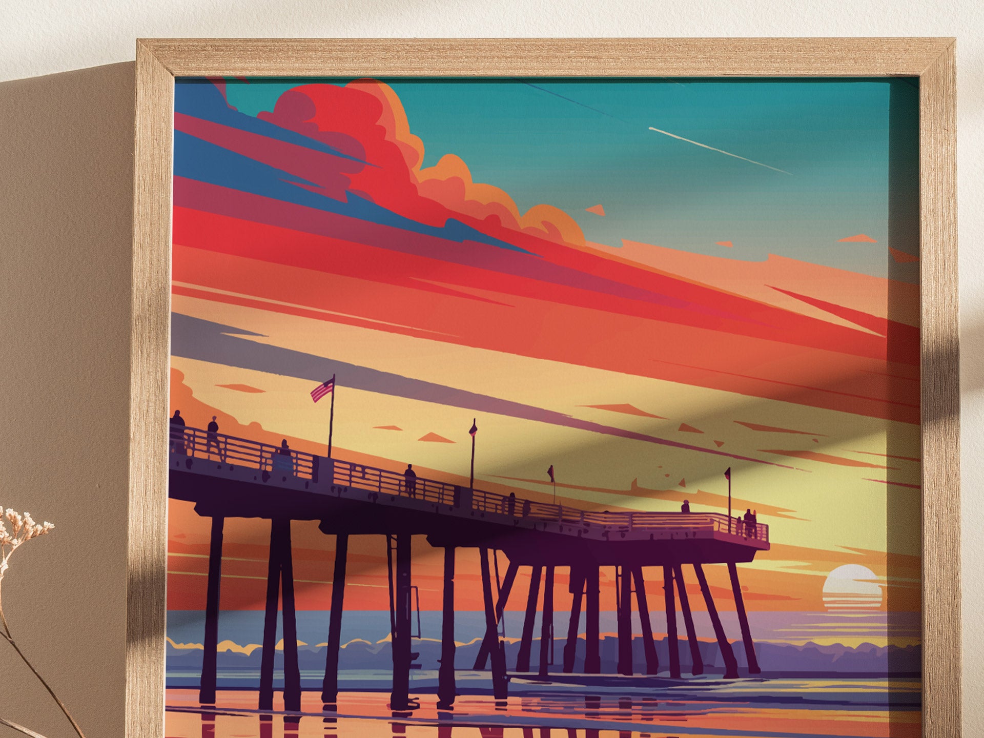 A framed artwork depicts a vibrant sunset over a pier, with silhouetted figures and colorful clouds in shades of orange, pink, and blue, reflecting on calm water.