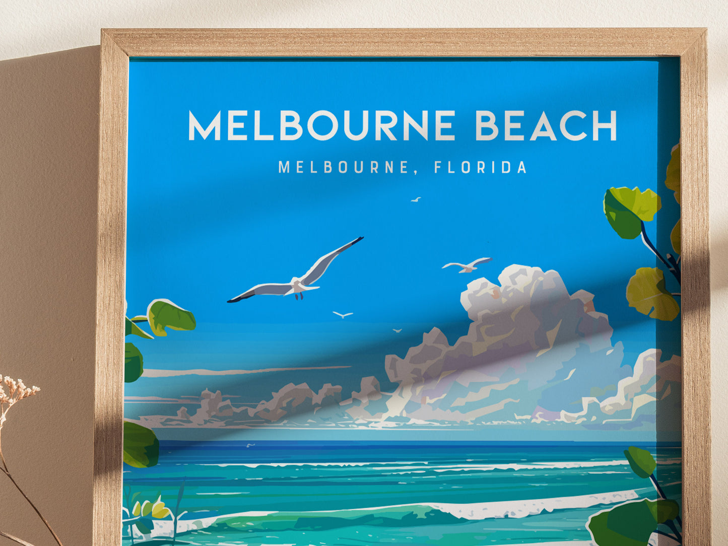 A framed poster depicting Melbourne Beach, Florida, features a vibrant blue sky, seagulls, ocean waves, and lush green foliage, creating a serene coastal scene.