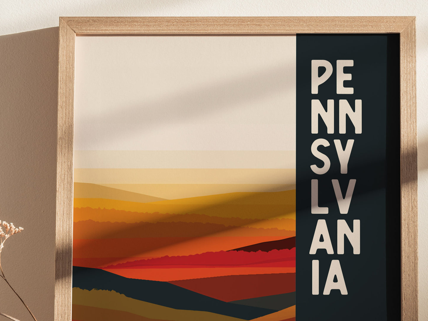 A framed poster features abstract, layered landscapes in warm tones with PENNSYLVANIA written vertically in bold letters. The sunlight casts a shadow on the textured wall.