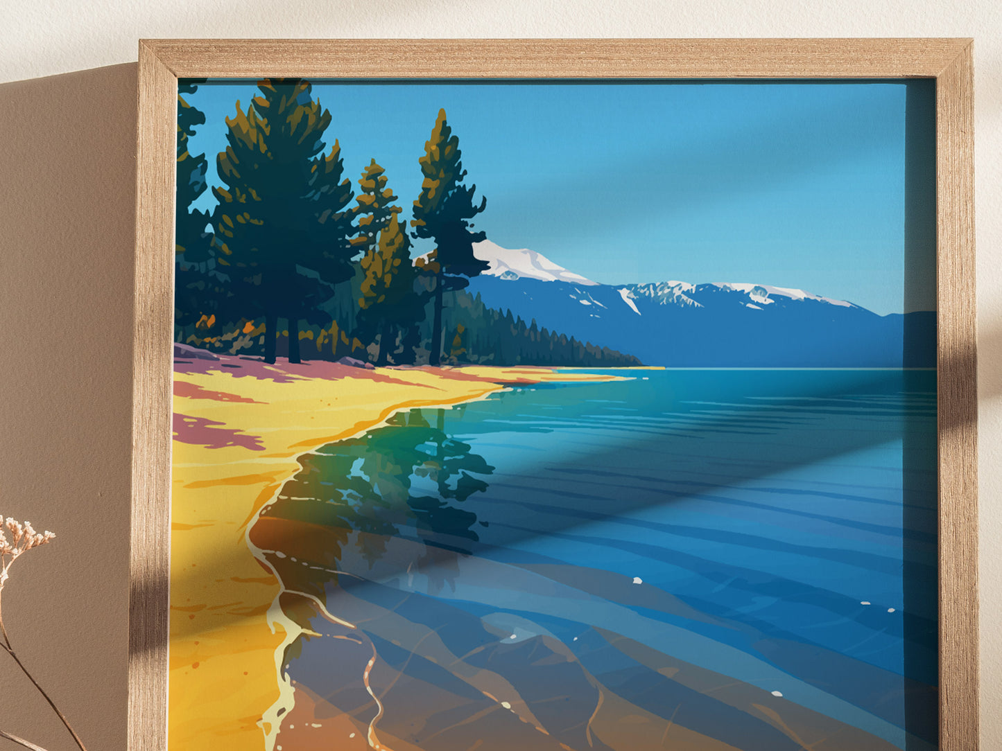 Framed artwork depicting a serene lakeside scene with clear blue waters, golden sandy beach, and lush pine trees against a backdrop of snow-capped mountains under a bright blue sky.
