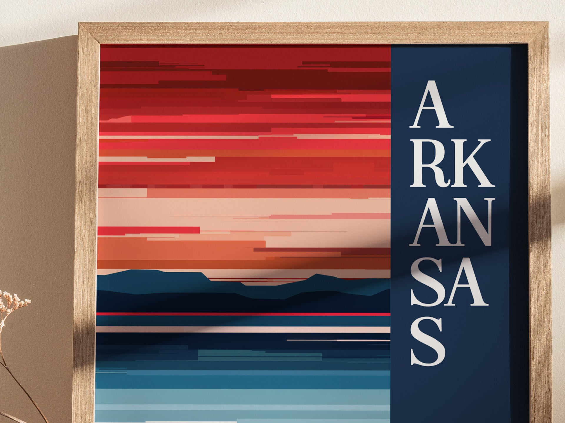 A framed abstract poster features bold horizontal stripes in red, orange, and blue, with ARKANSAS in vertical white text on a dark blue background. A dried flower is visible nearby.