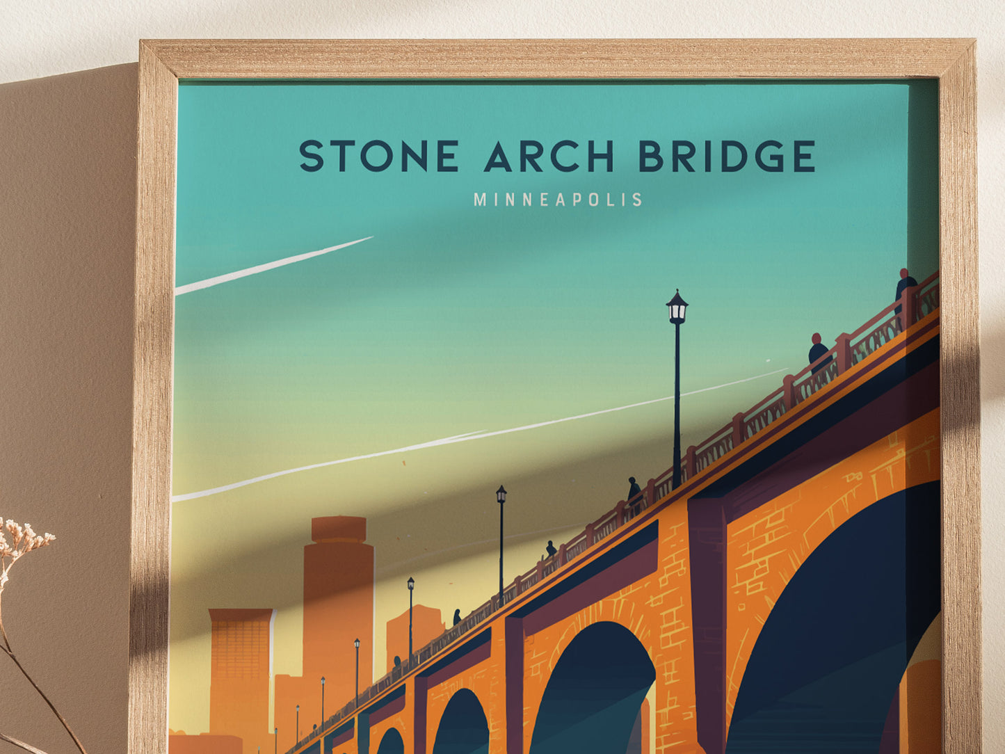 A framed poster depicts the Stone Arch Bridge in Minneapolis, silhouetted figures walking across it, and a stylized city skyline under a vibrant, gradient sky.