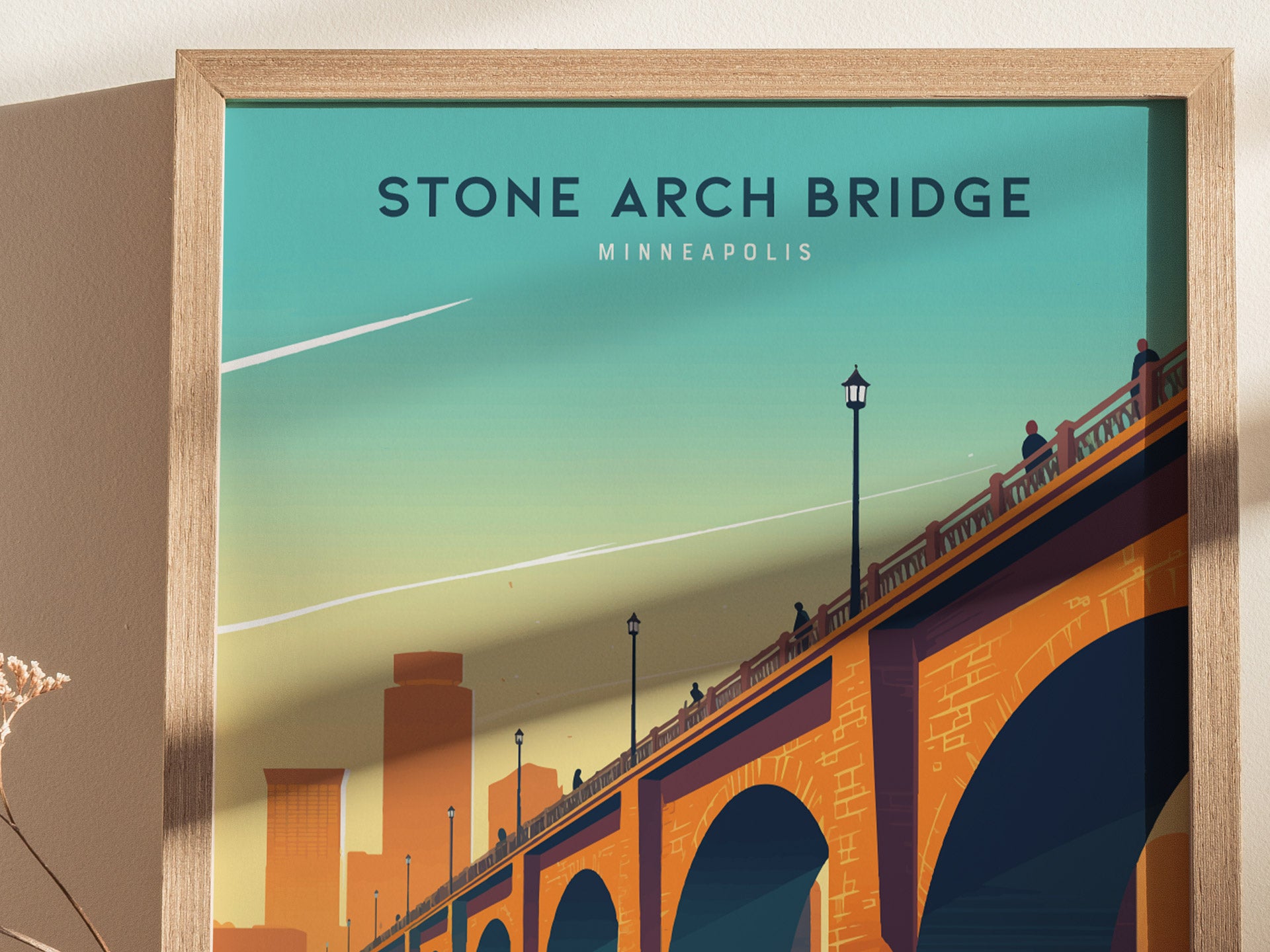 A framed poster depicts the Stone Arch Bridge in Minneapolis, silhouetted figures walking across it, and a stylized city skyline under a vibrant, gradient sky.
