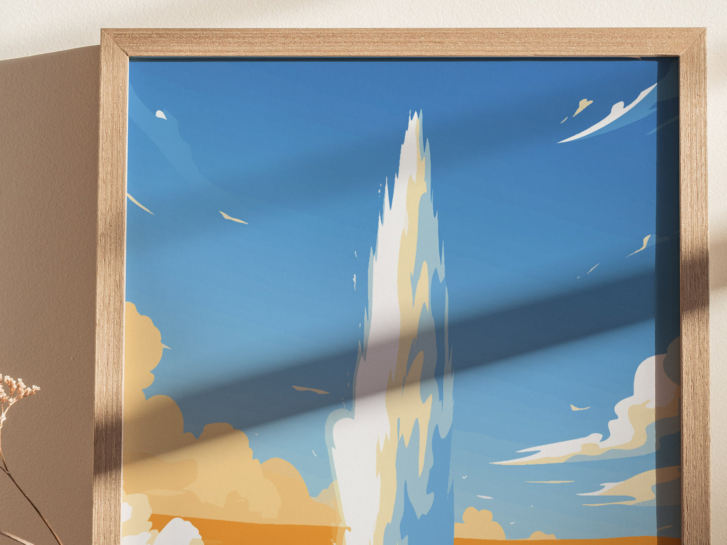 A framed poster depicting a stylized eruption of Old Faithful Geyser against a bright blue sky, with abstract clouds and a wooden frame casting a shadow.