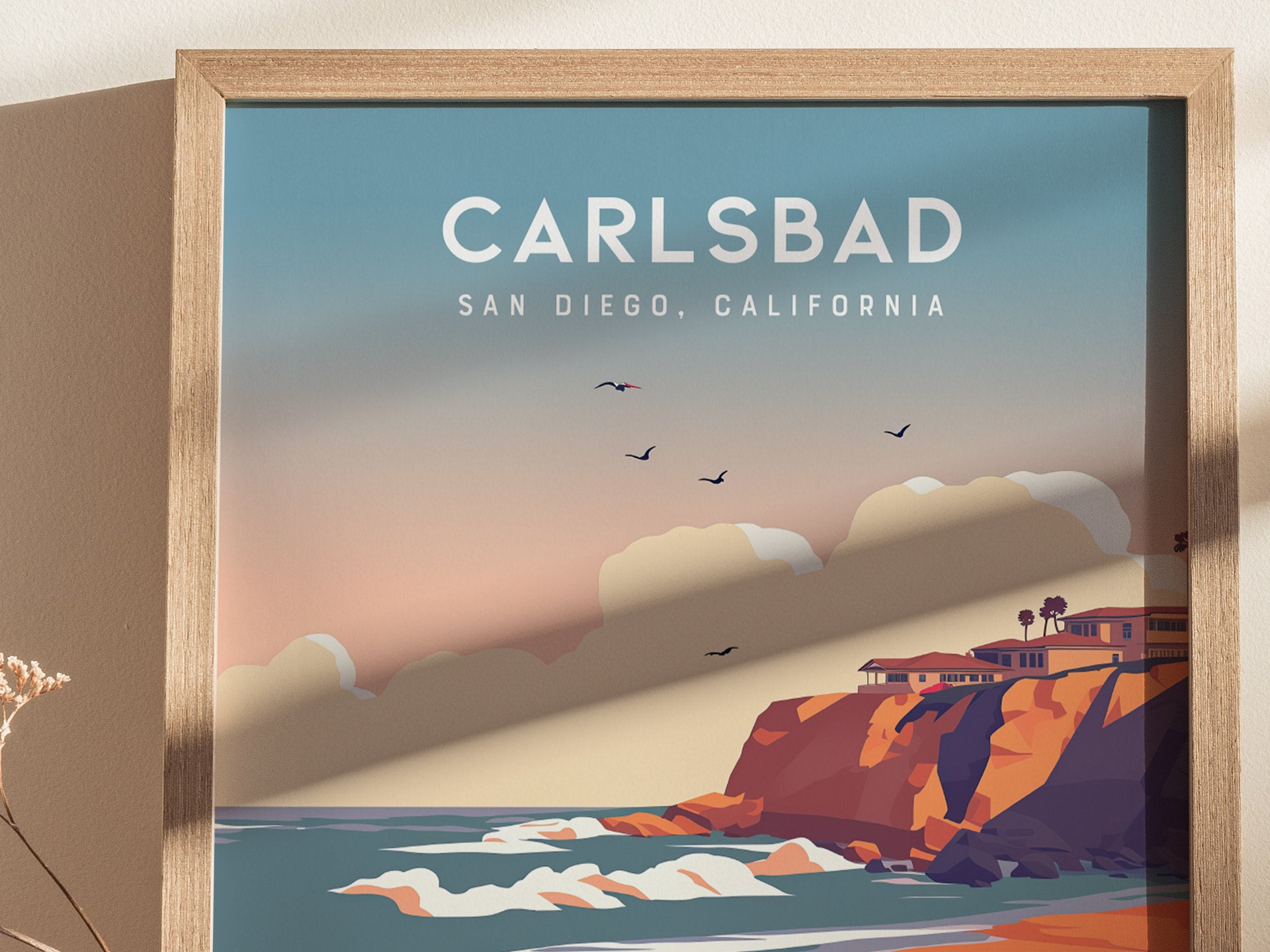 Framed poster featuring Carlsbad, San Diego, California, with colorful cliffs, ocean waves, and silhouetted birds against a pastel sky. The artwork captures a serene coastal scene.
