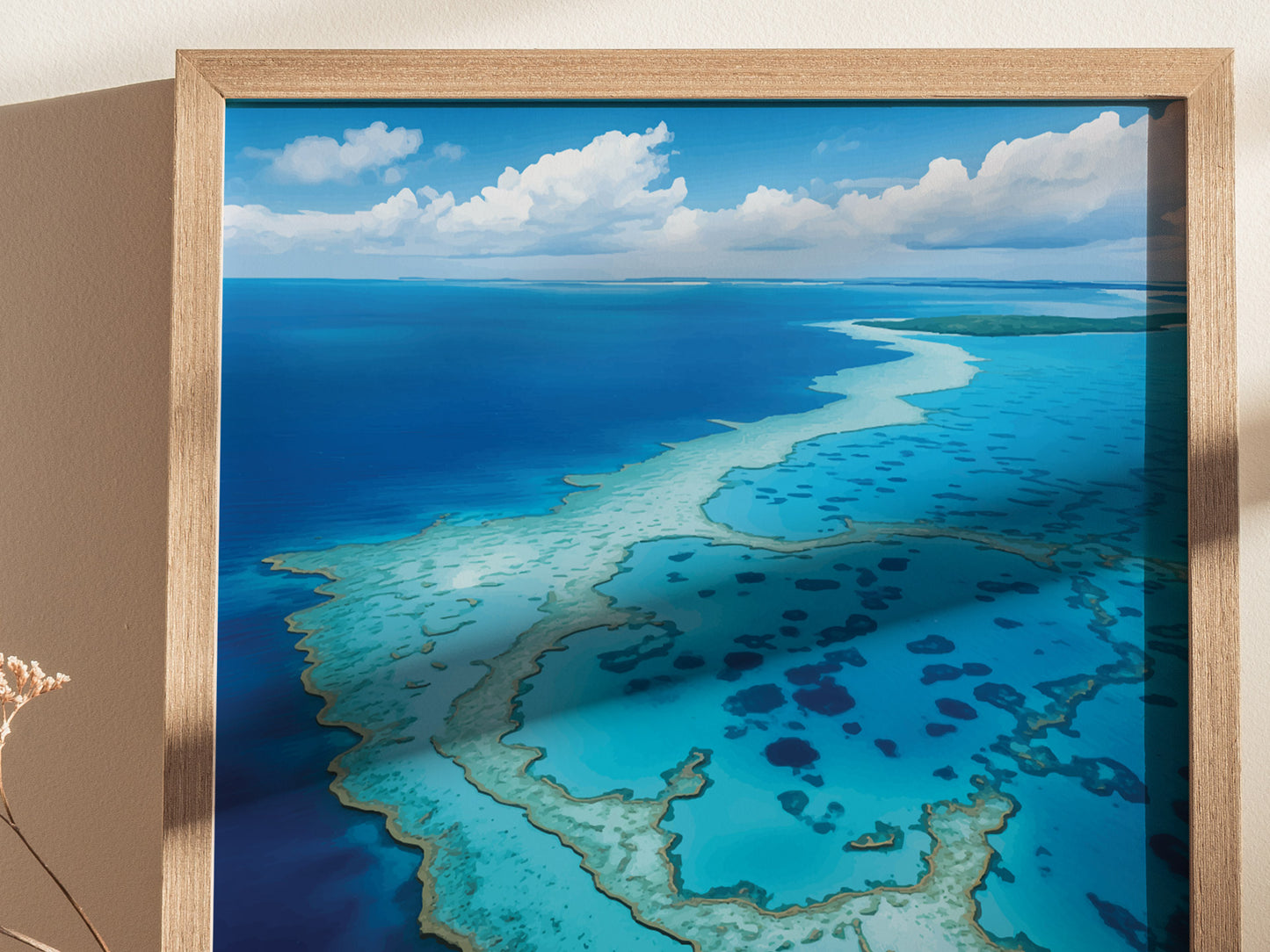 A framed art print depicts the Great Barrier Reef, showcasing vibrant turquoise waters and intricate coral formations under a partly cloudy sky. The artwork is displayed against a neutral wall.