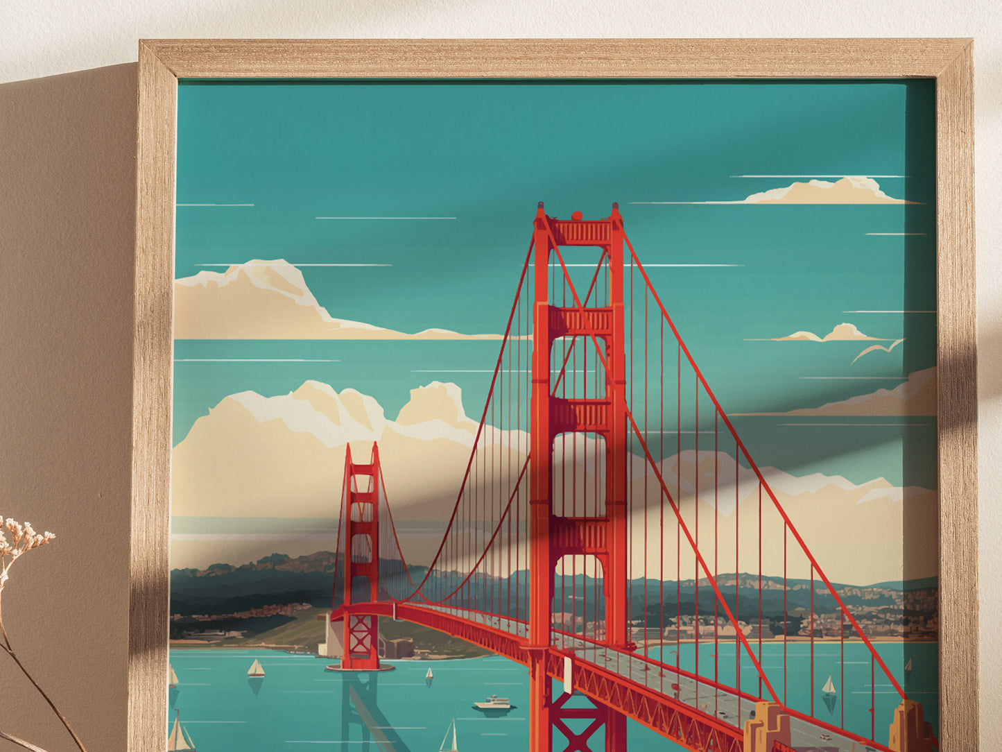 A framed poster featuring the Golden Gate Bridge in vibrant red against a turquoise sky and distant mountains, with sailboats on the water below.