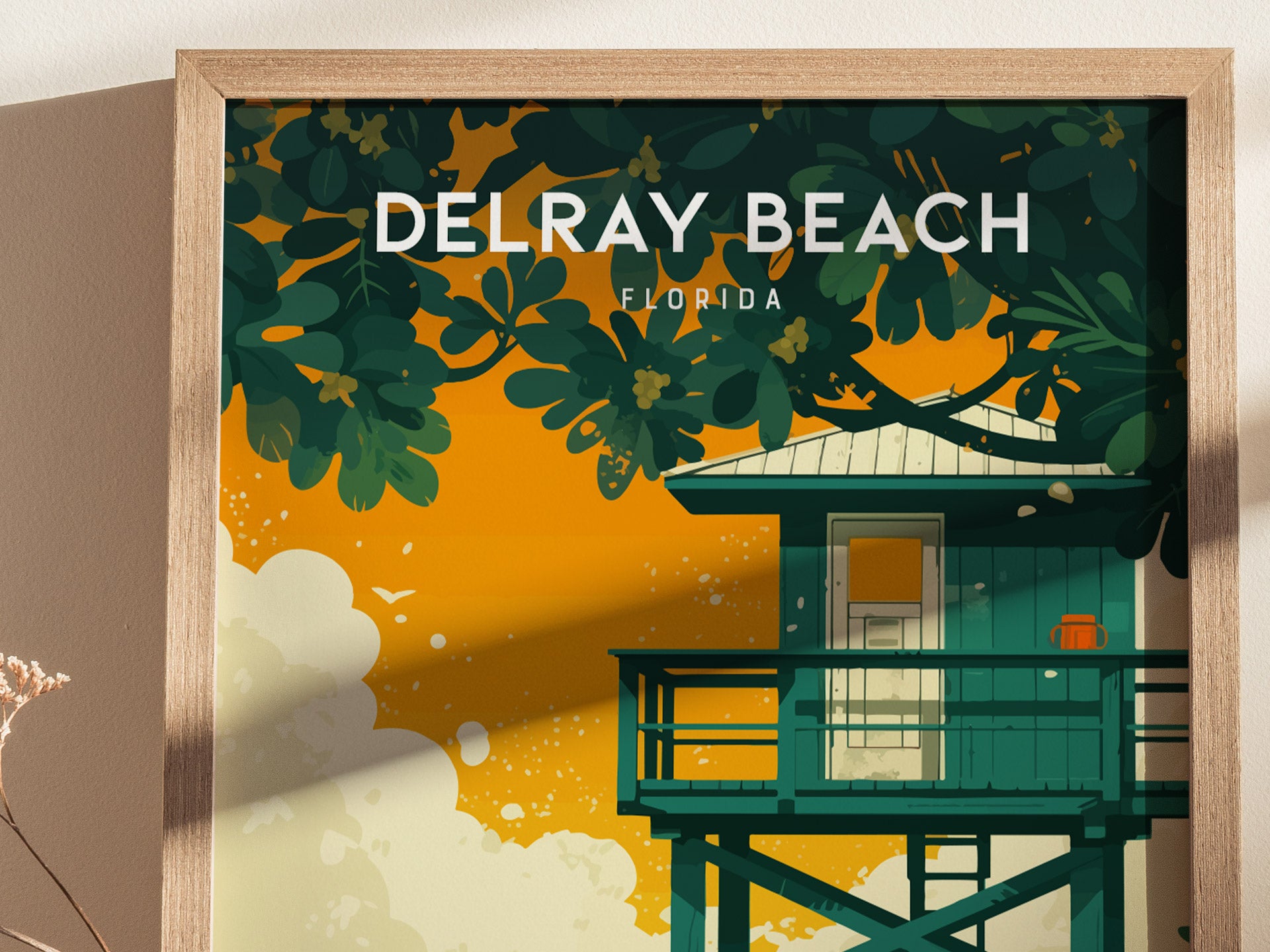 A framed Delray Beach poster features a turquoise lifeguard stand with lush green foliage against a vibrant orange sky. The artwork evokes a tropical coastal atmosphere.