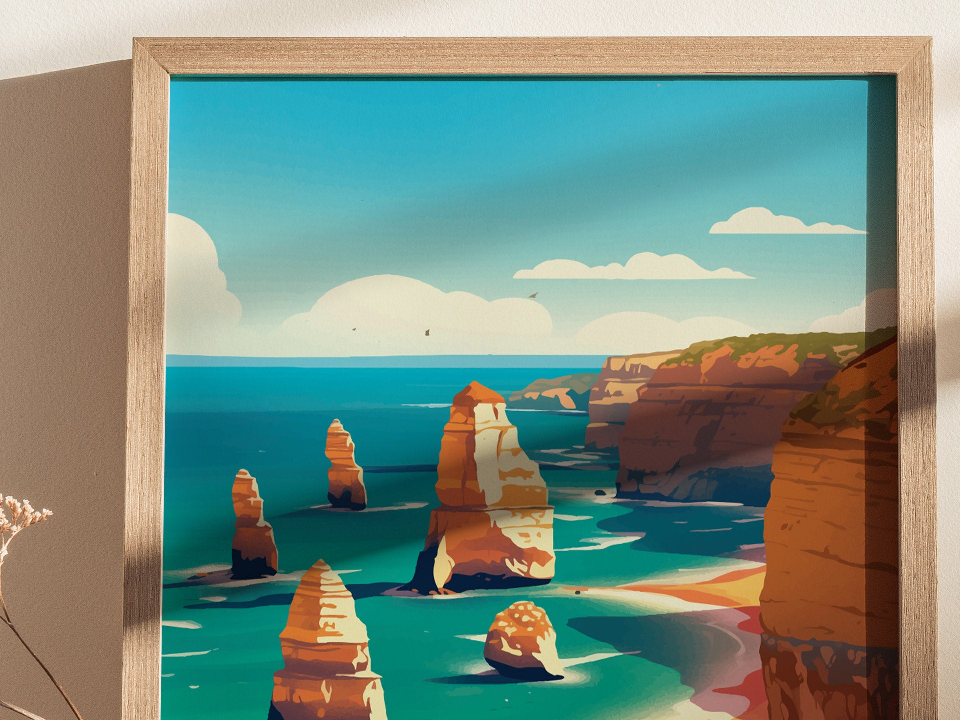 A framed poster depicts the Twelve Apostles, featuring towering limestone stacks against a vibrant blue ocean and sky, with coastal cliffs in the background. The scene conveys natural beauty.