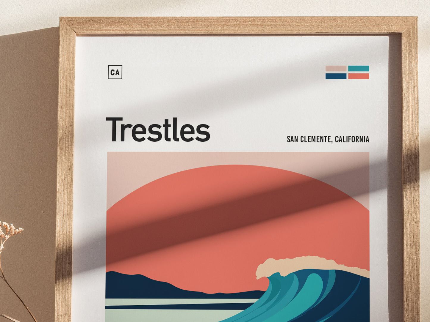 A framed poster features minimalist artwork of a wave against a sunset with the text Trestles, San Clemente, California. Sunlight casts shadows on the poster.