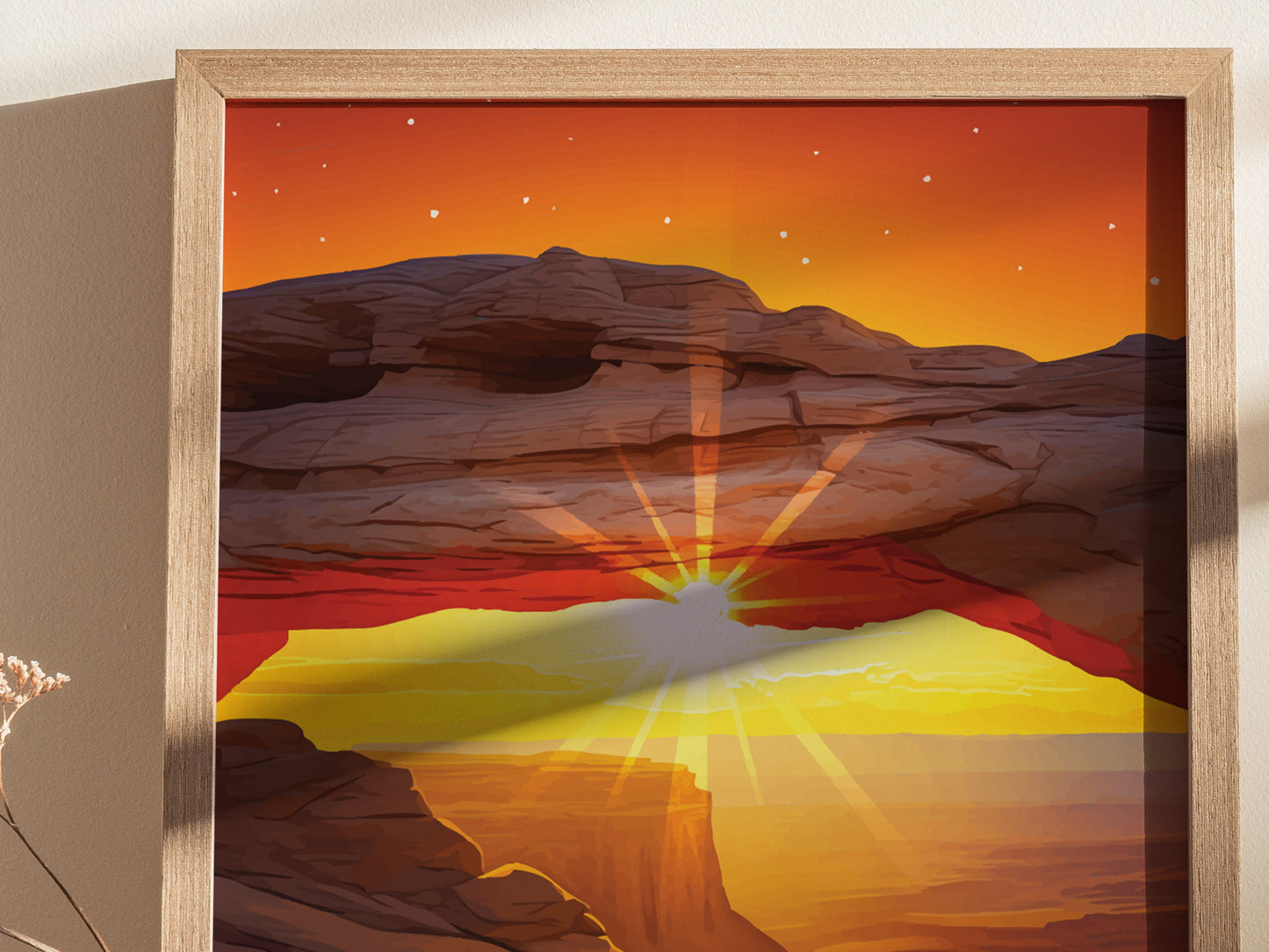 Framed artwork depicting a vibrant sunset over a rocky arch formation with a starry sky, casting golden rays across a desert landscape. The poster is propped against a beige wall.