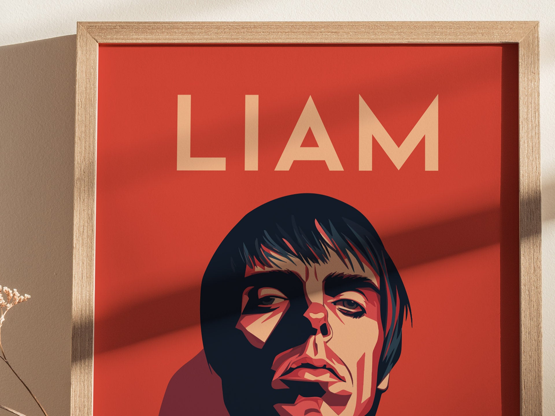 A framed poster with a stylized portrait on a red background, featuring the word LIAM in bold letters above. The image casts a shadow on the adjacent wall.
