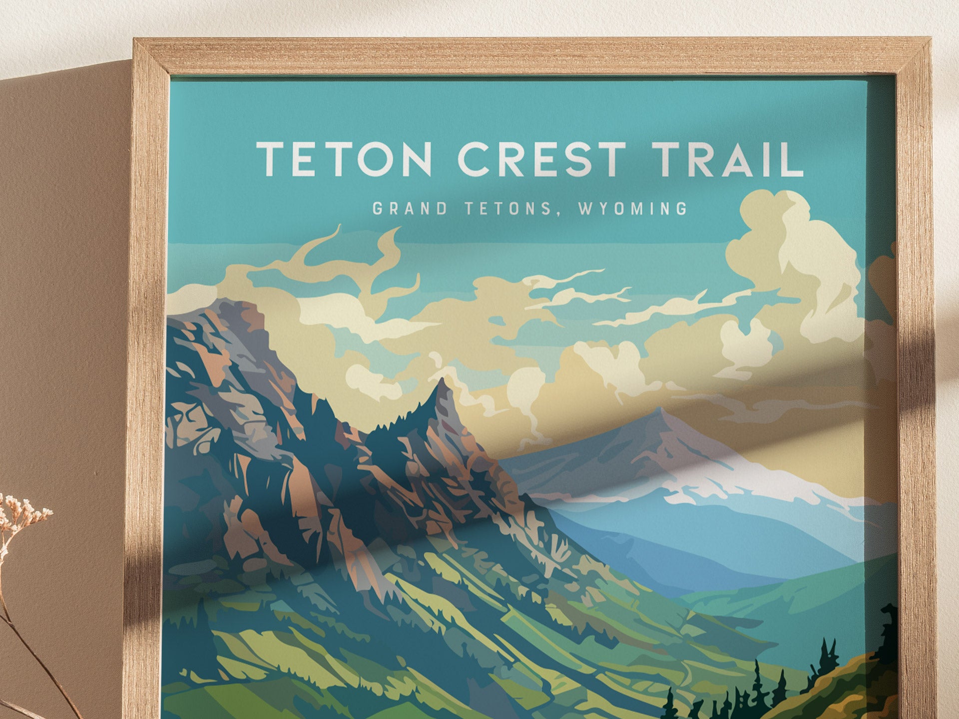 Framed Teton Crest Trail poster featuring stylized illustrations of jagged mountain peaks and cloud-filled skies. The text reads Teton Crest Trail, Grand Tetons, Wyoming against a blue background.