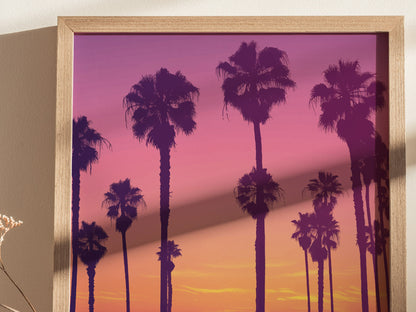 Framed poster featuring silhouetted palm trees against a vibrant sunset with hues of purple, pink, and orange. The artwork captures a serene and picturesque evening scene.