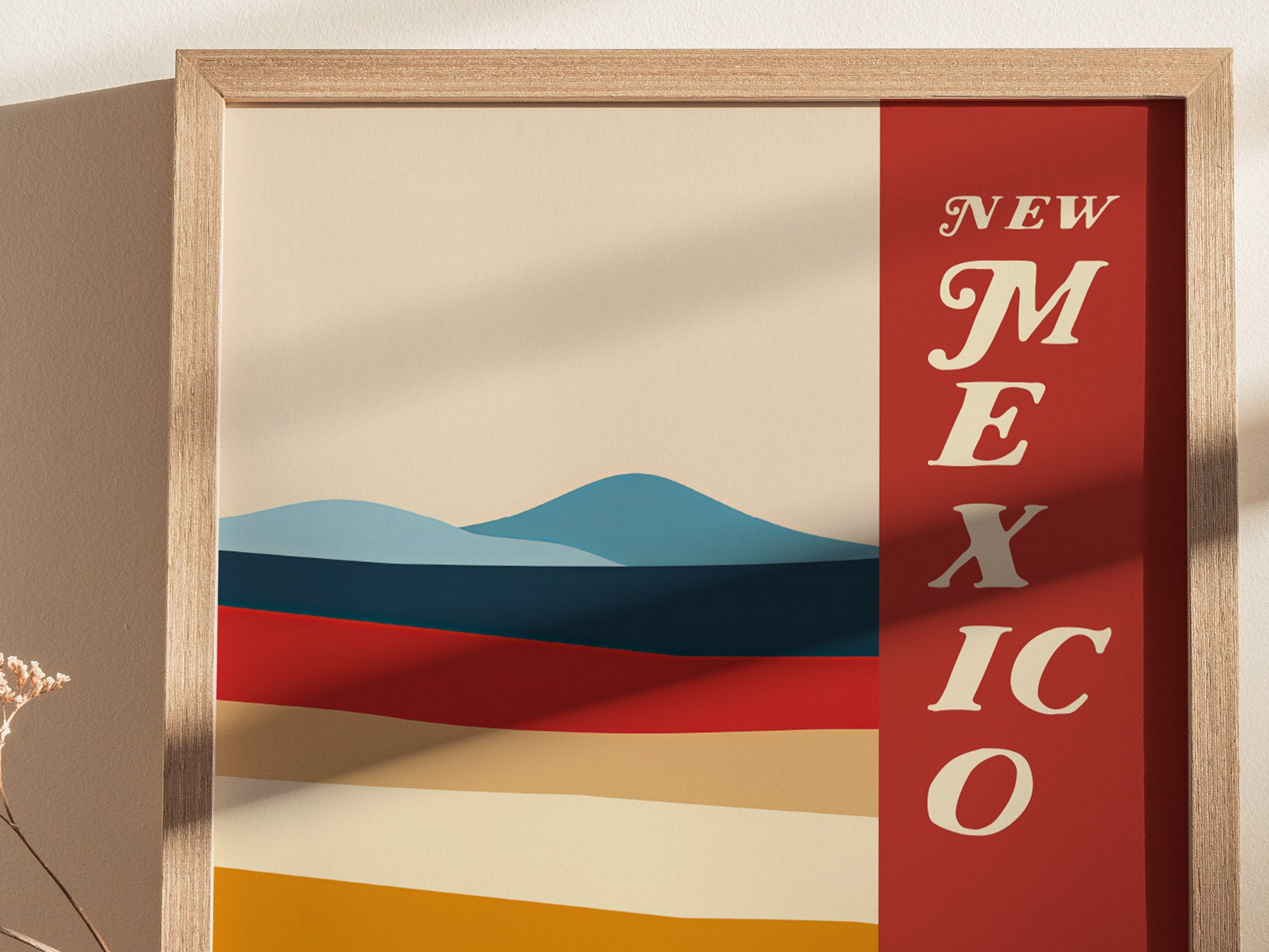 A framed poster featuring bold, colorful stripes representing desert landscapes with the words New Mexico in elegant typography on a red background. The design includes blue mountains.