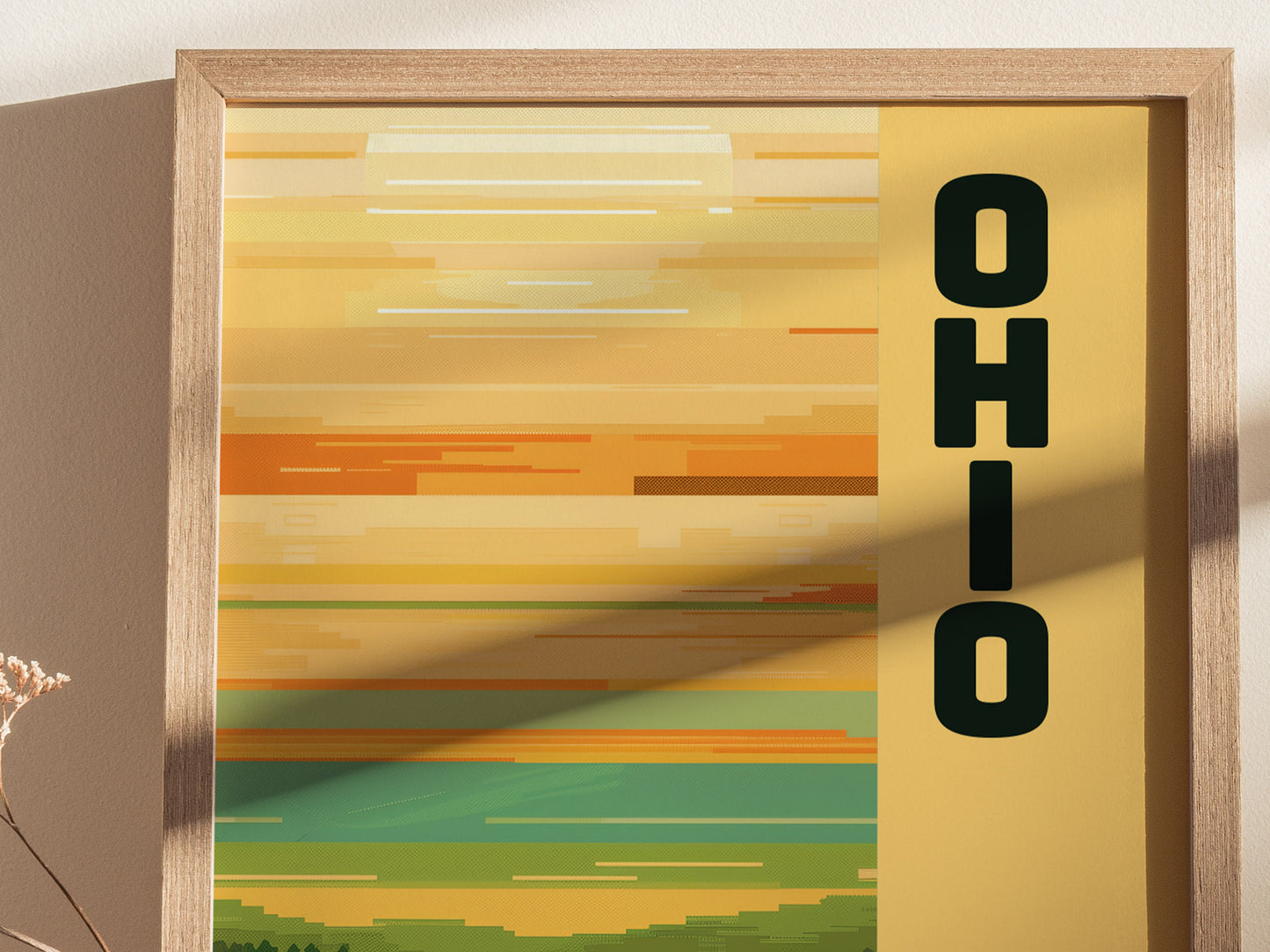 A framed poster with horizontal, minimalist stripes in warm yellow and orange hues features the word OHIO vertically on the right. Soft shadows add depth to the composition.