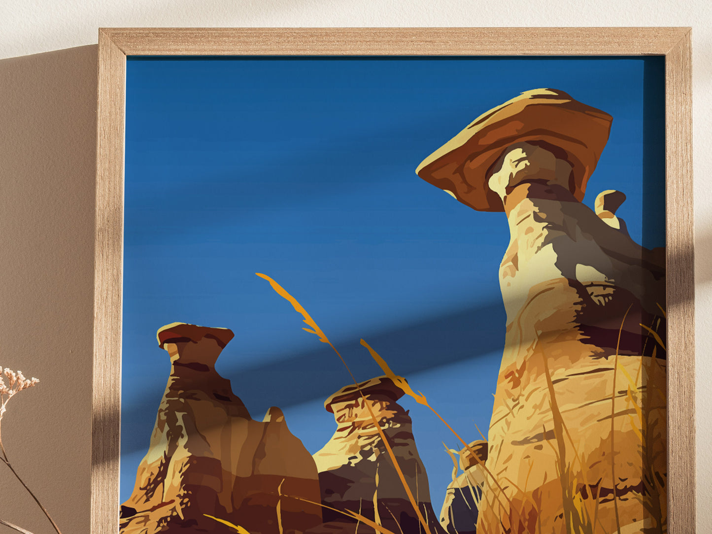 Framed artwork depicting towering hoodoos against a clear blue sky, with golden grasses in the foreground, capturing the essence of a rugged desert landscape.