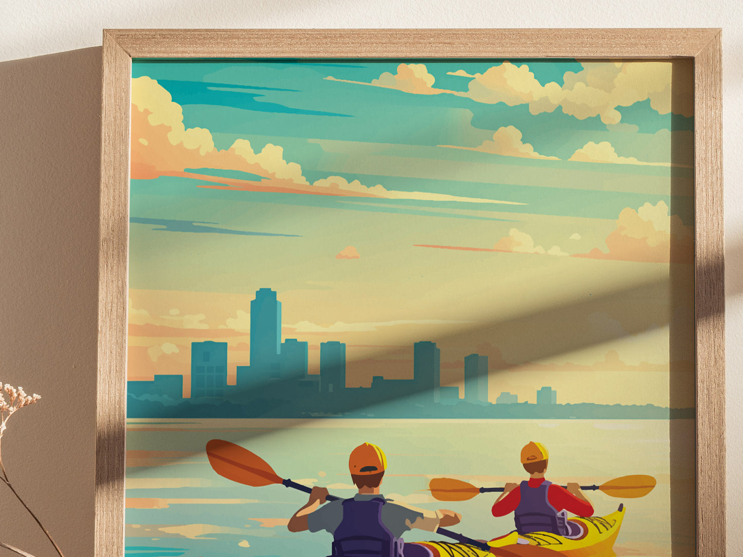 Illustration of two kayakers paddling on calm waters with a city skyline in the background, under a colorful sky. The artwork is framed in a light wooden frame.