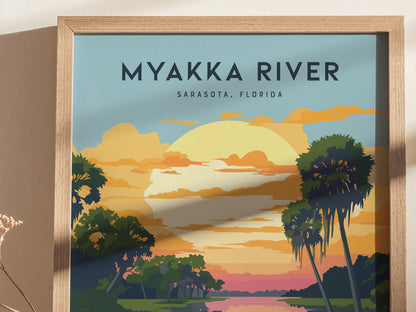 A framed poster depicting Myakka River with a vibrant sunset, palm trees, and a serene river scene. The text MYAKKA RIVER, SARASOTA, FLORIDA is prominently displayed at the top.