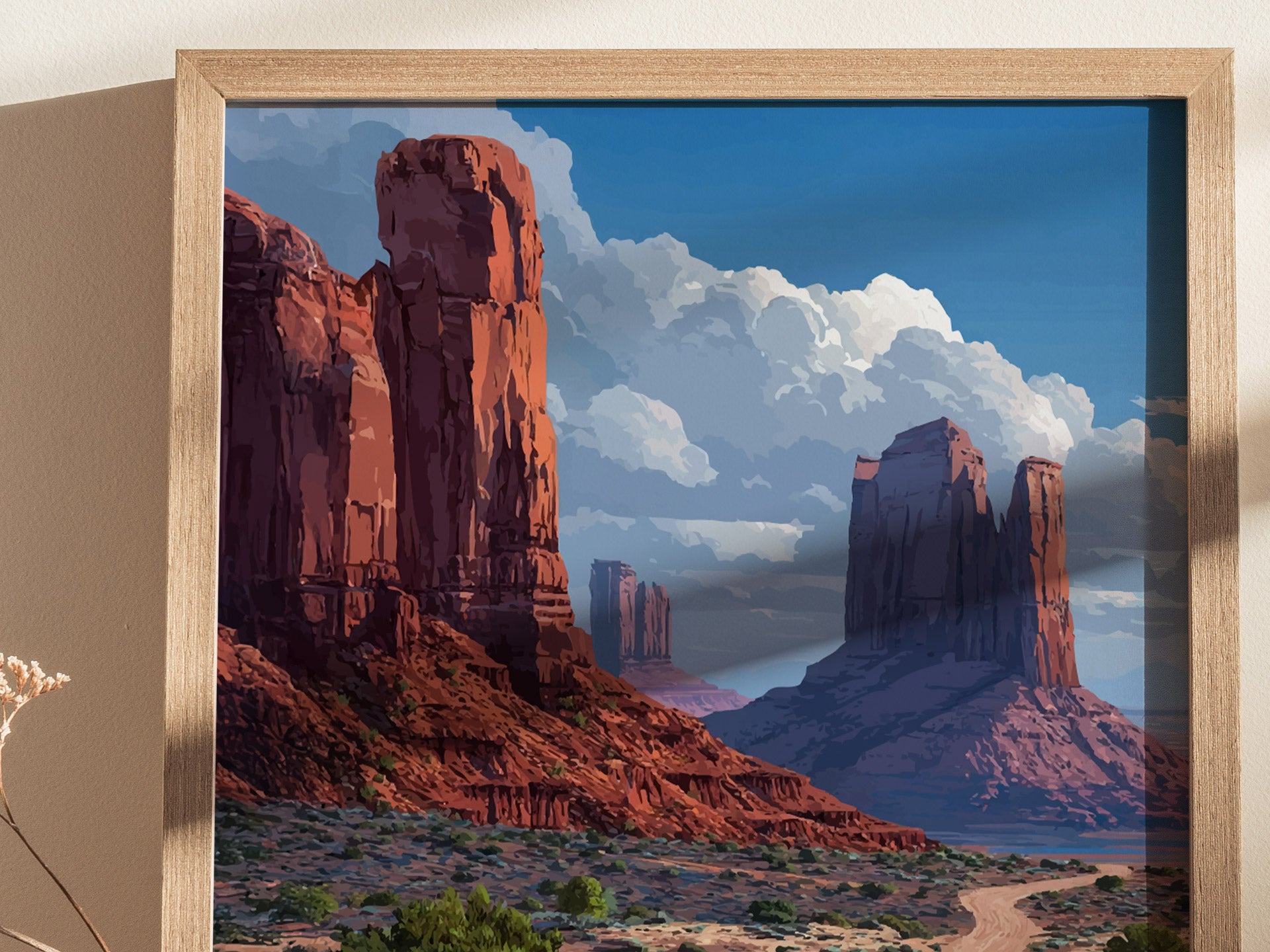 A framed poster of Monument Valley depicts red sandstone mesas under a vibrant blue sky with scattered clouds. The iconic buttes and desert landscape create a striking visual impression.