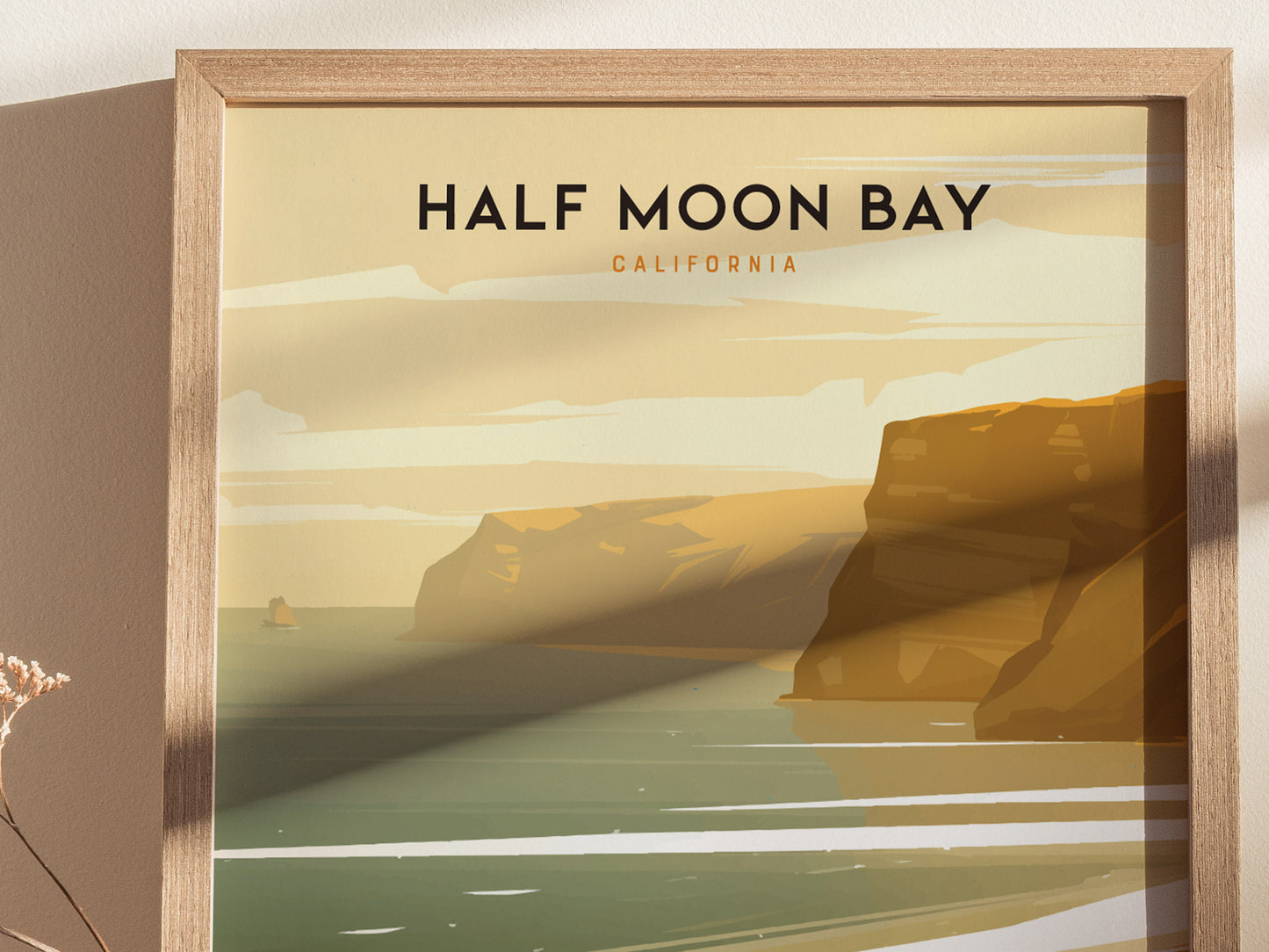Framed poster featuring an illustration of Half Moon Bay, California, depicting golden cliffs and serene ocean waves under a soft, pastel sky. Shadows cast on the wall add depth.