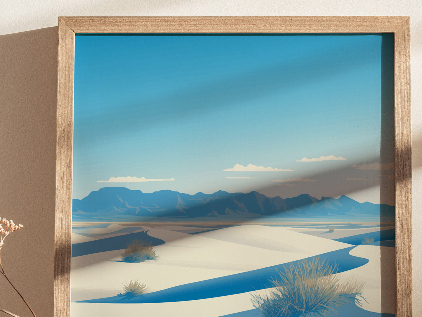 Framed artwork depicting White Sands National Park with rolling white dunes and distant blue mountains under a clear sky. Sunlight casts a shadow on the image, creating a serene atmosphere.