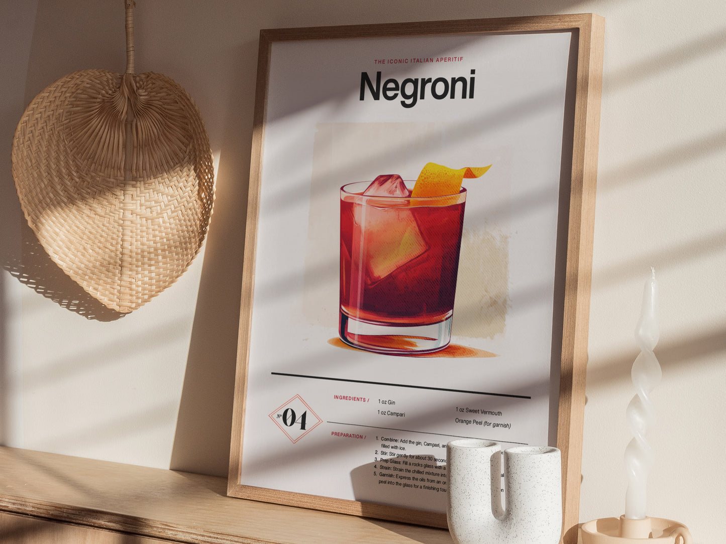 A framed Negroni cocktail poster is displayed on a wooden shelf with a woven fan and a twisted white candle nearby, creating a cozy atmosphere.
