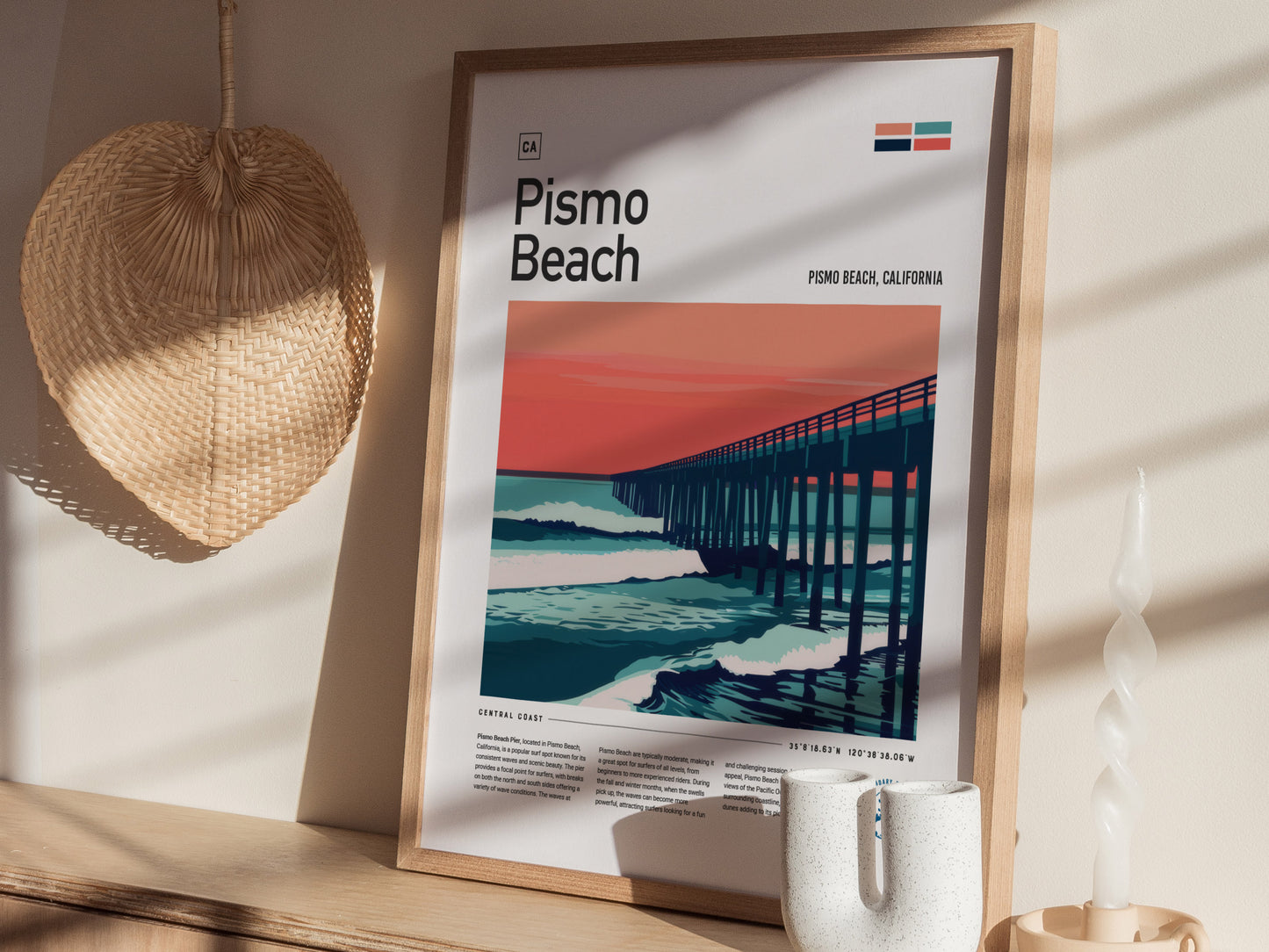 A framed Pismo Beach poster depicting a pier against a vibrant sunset is displayed on a wooden shelf, accompanied by a woven basket and a white twisted candle.