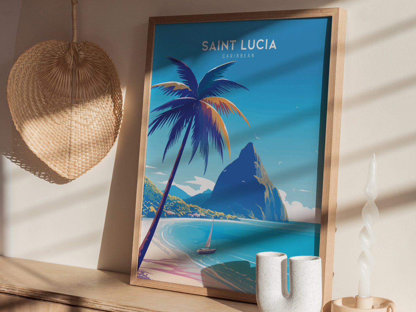 A framed poster of Saint Lucia featuring a beach scene with palm trees and the Pitons, displayed on a wooden shelf with a woven wall hanging and decorative candle nearby.