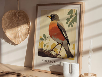 A framed illustration of an American Robin is displayed on a wooden shelf, accompanied by a woven wall decor and a twisted white candle.
