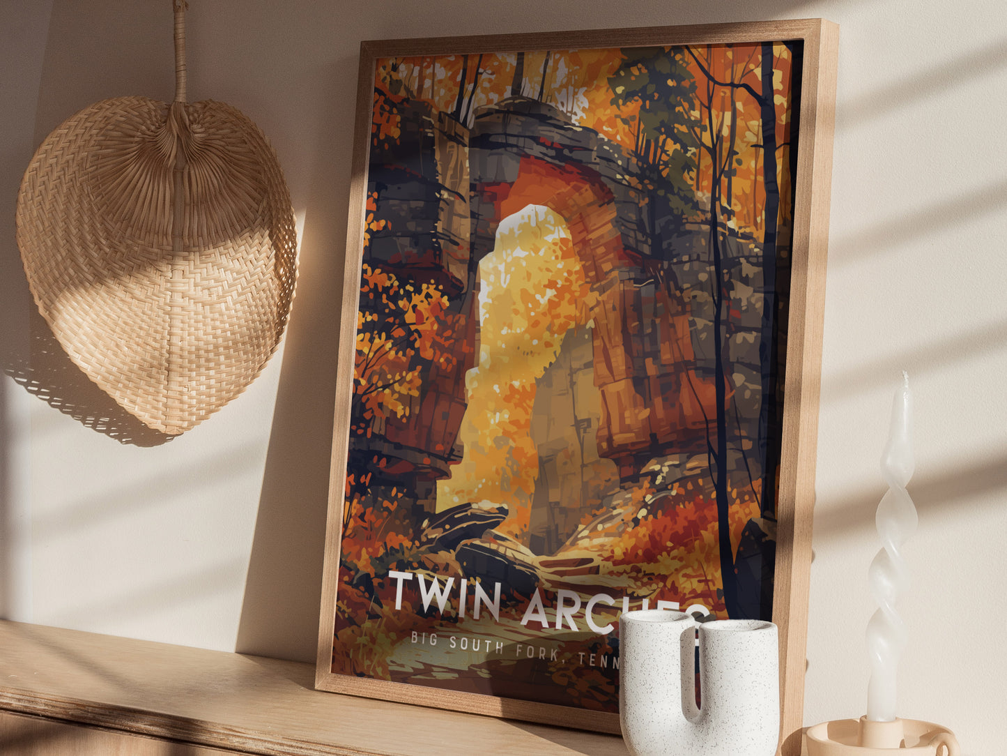 A framed poster of Twin Arches with vibrant autumn foliage is displayed on a wooden shelf, next to a woven basket and a twisted white candle.