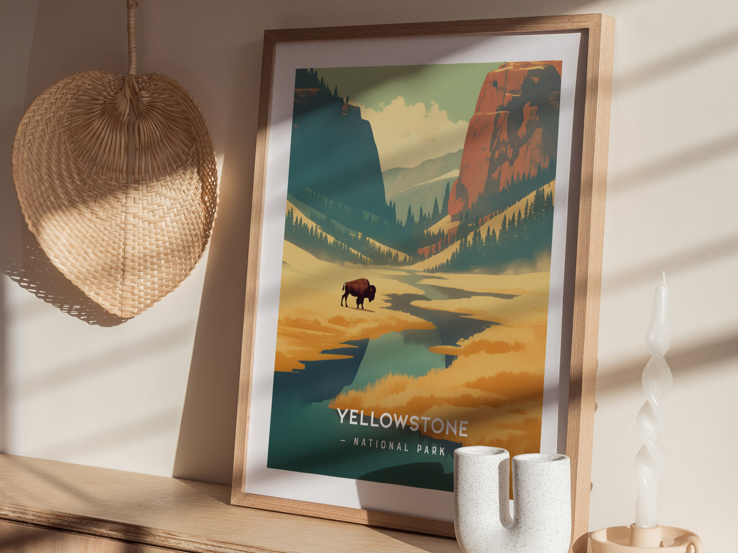 Framed Yellowstone National Park poster featuring a stylized landscape with a bison, mountains, and forests. Displayed on a shelf with a wicker basket and decorative candle.