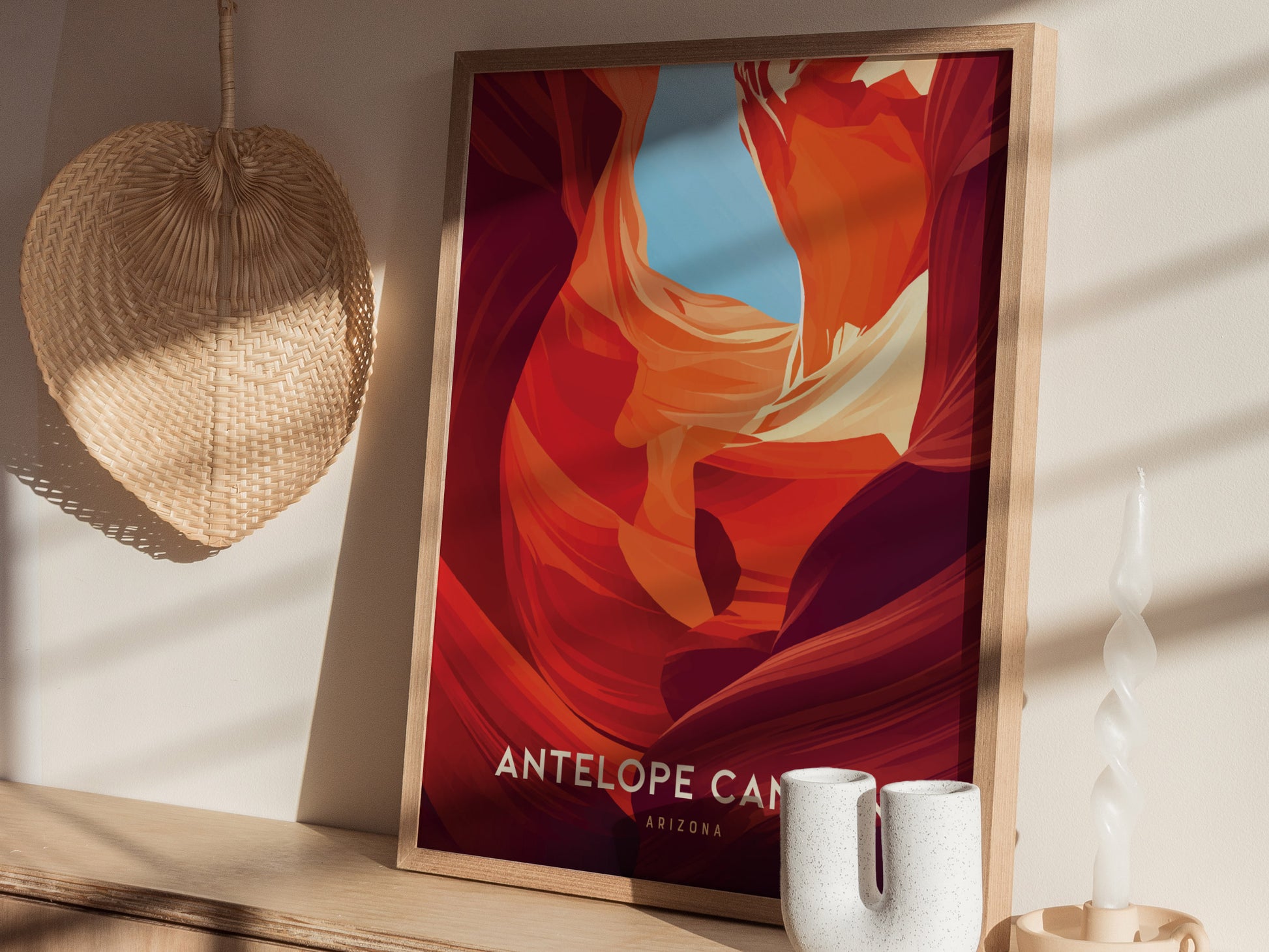 A framed poster of Antelope Canyon with vibrant red and orange sandstone formations is displayed on a shelf with a woven fan, a twisted candle,.