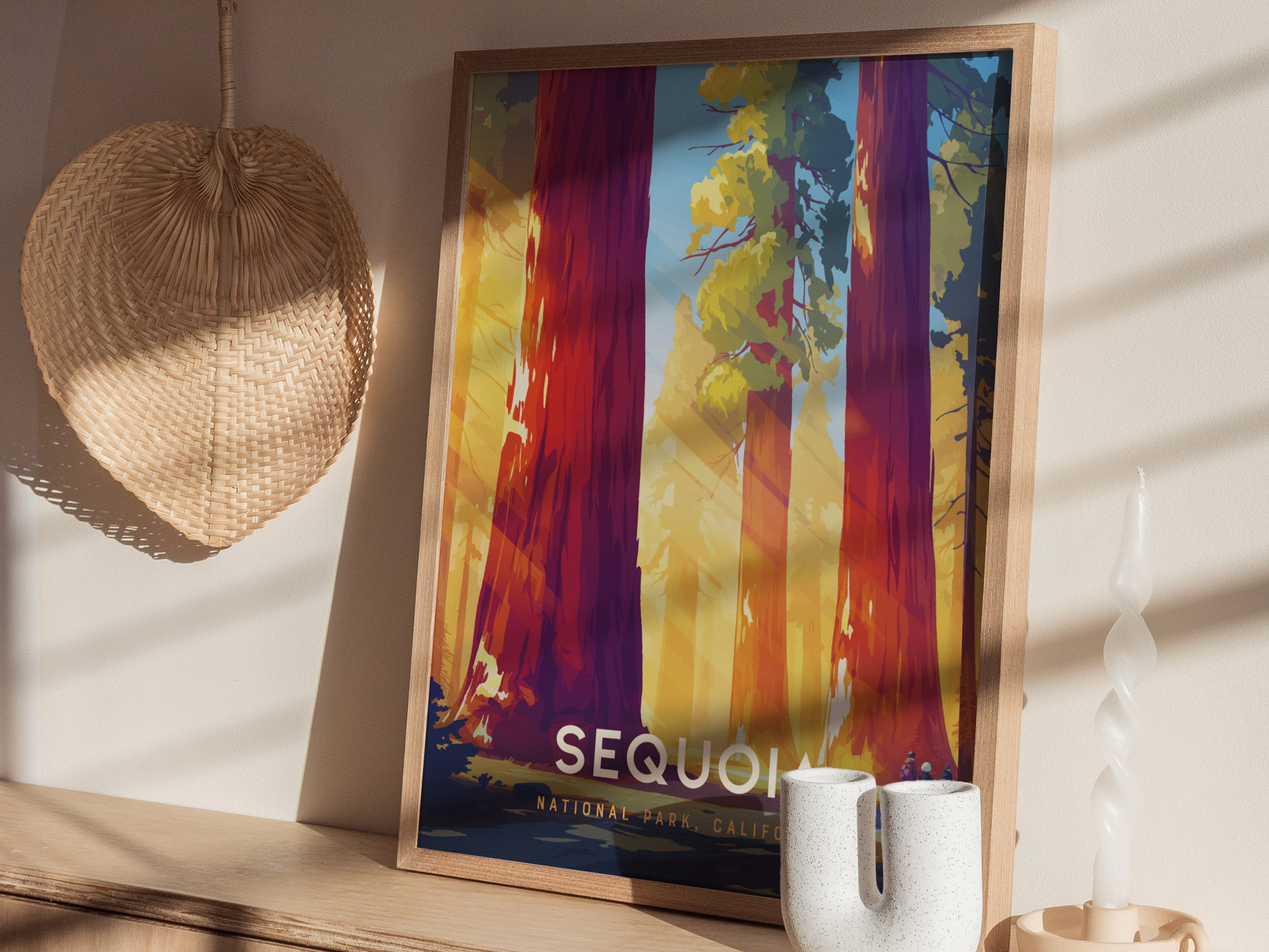 Framed artwork depicting colorful, towering sequoia trees under sunlight is displayed on a wooden shelf, accompanied by a woven basket, a twisted candle, and a white ceramic vase.
