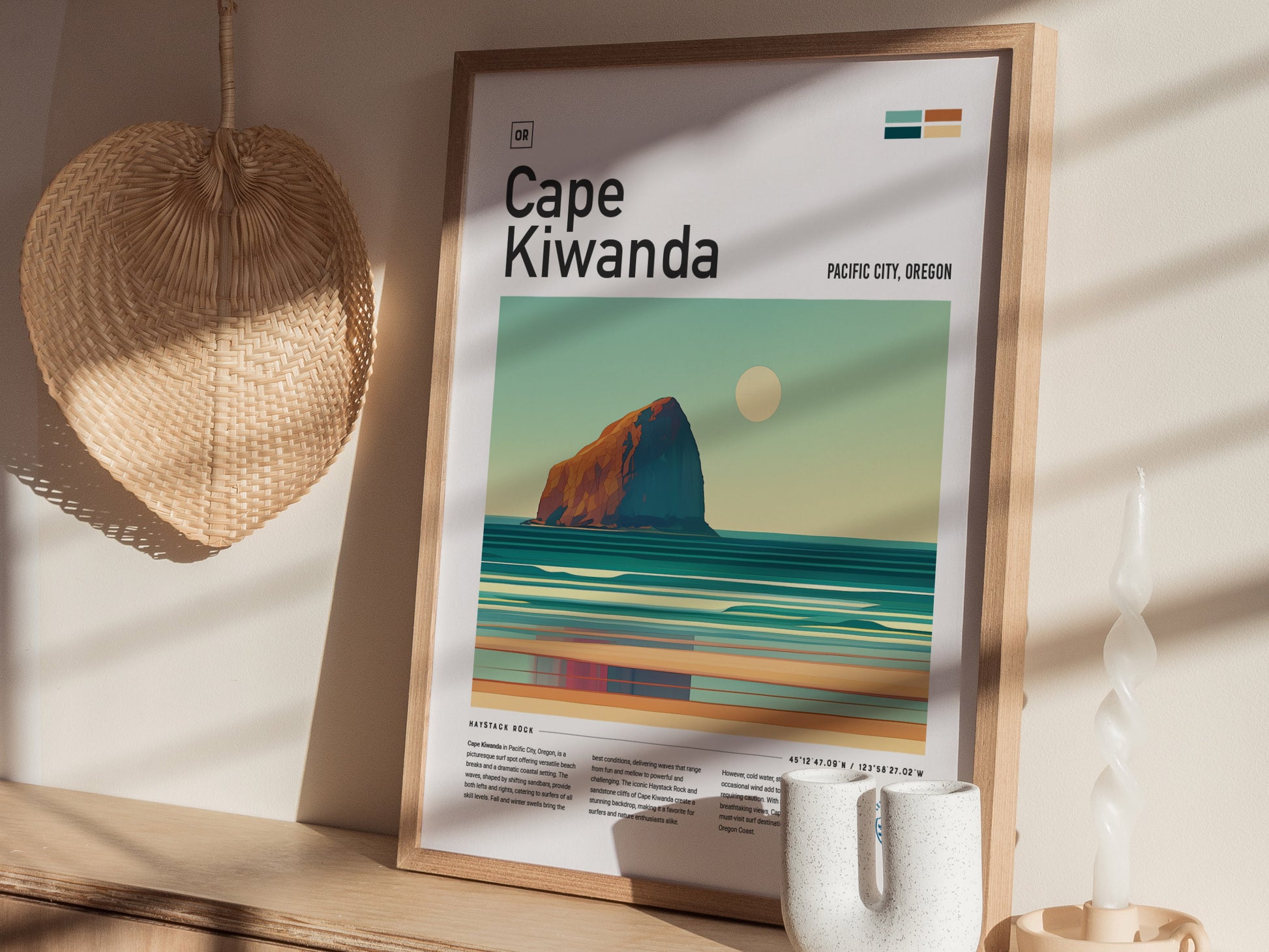 A framed Cape Kiwanda poster featuring an abstract depiction of Haystack Rock and ocean waves is displayed on a shelf. A woven wall decor and a twisted candle are nearby.